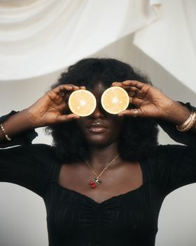 Artistic portrait of a woman holding lemon slices over her eyes, creating a playful expression.