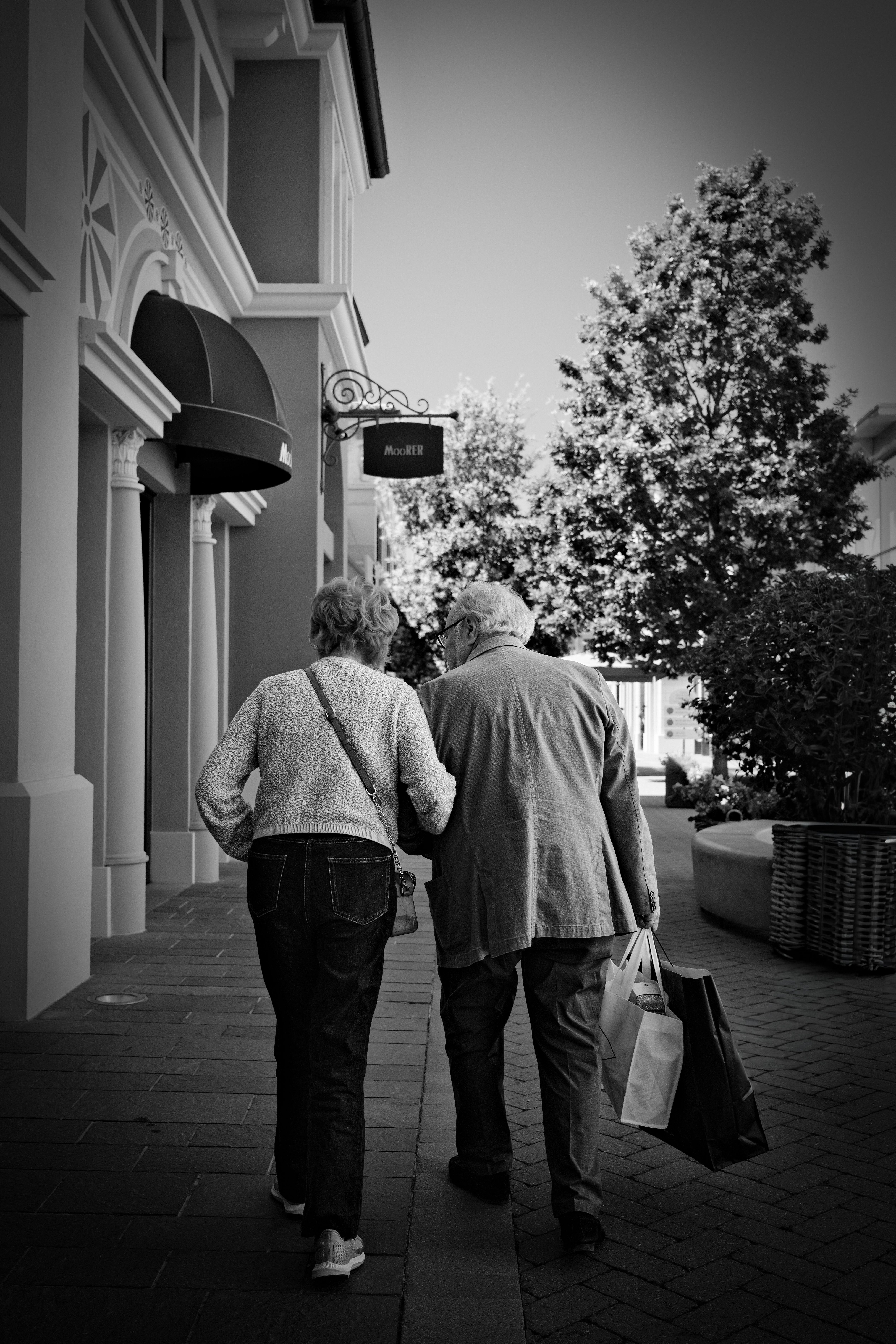 A senior couple strolls along a shopping street in Milan, Italy, carrying shopping bags.