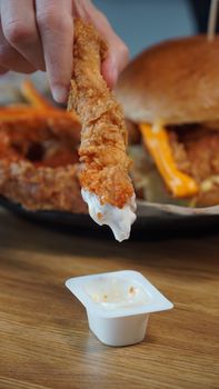 Close-up of a crispy chicken tender being dipped into a creamy sauce, perfect for fast food themes.