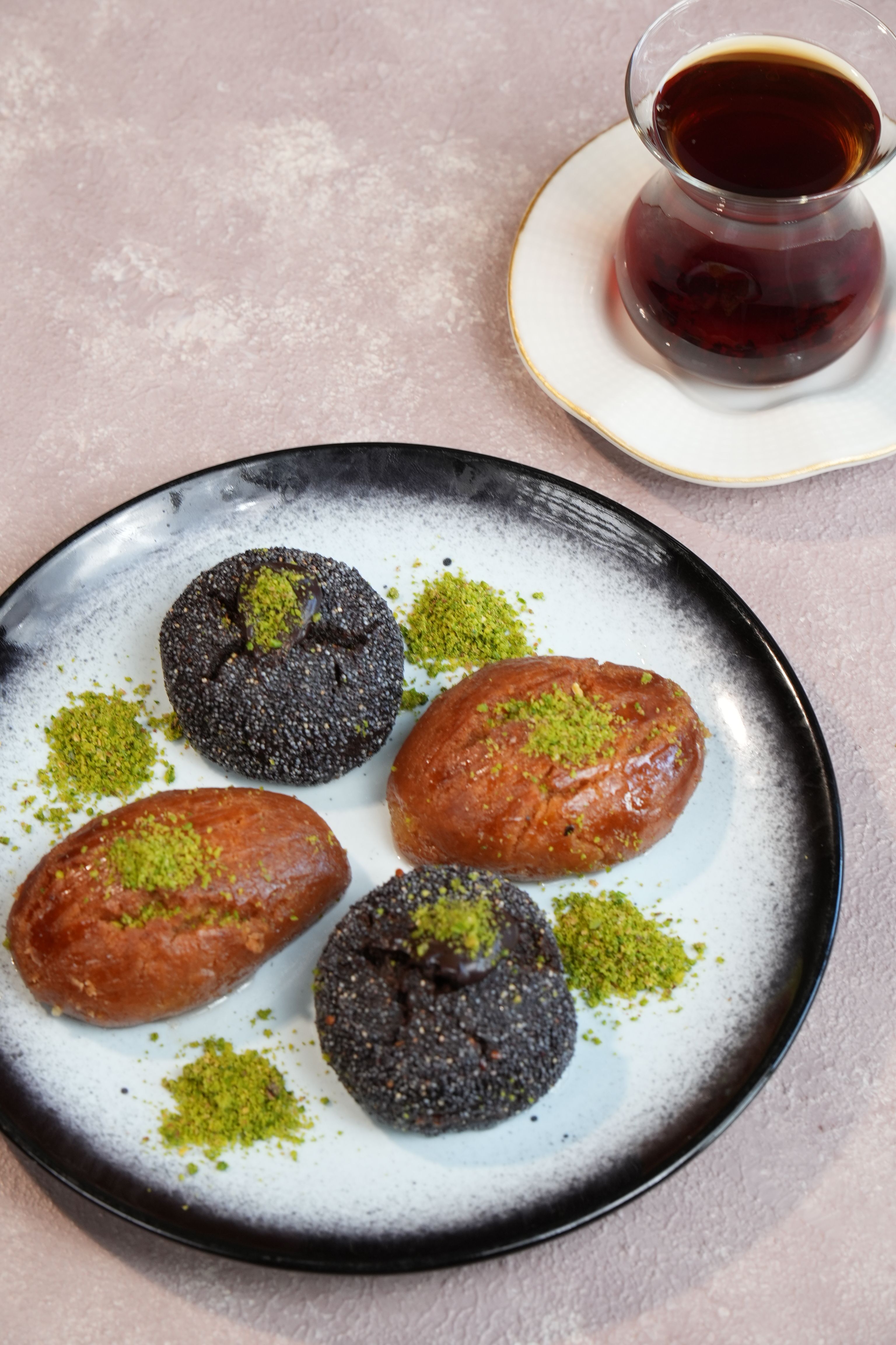 Plate of Turkish desserts topped with pistachio, served with a cup of black tea.
