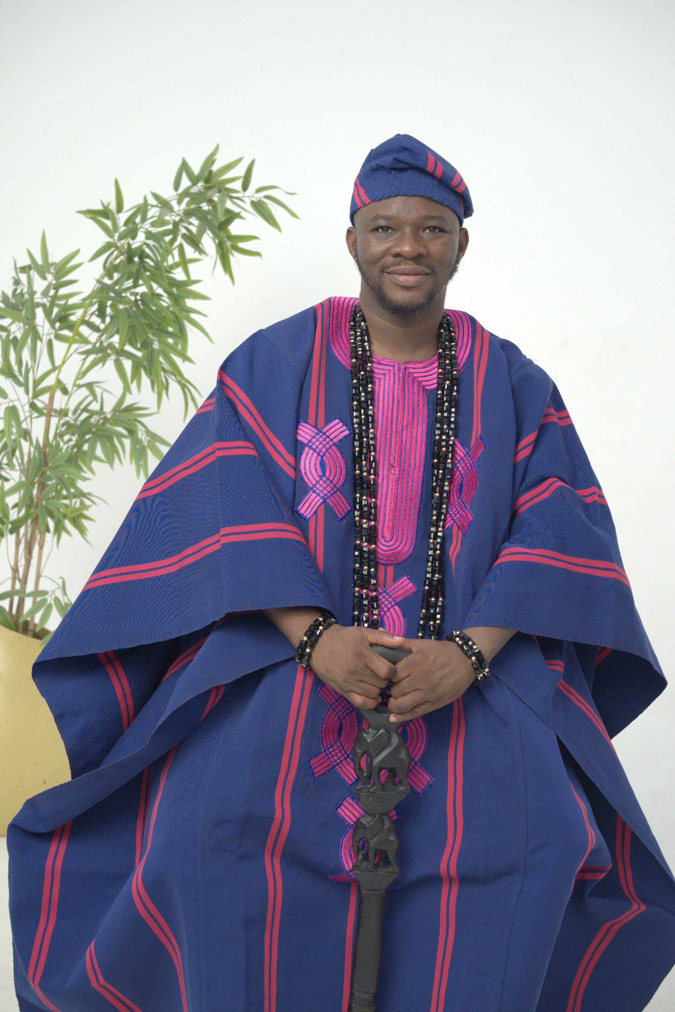 A man in traditional Yoruba attire poses indoors, showcasing Nigerian culture.