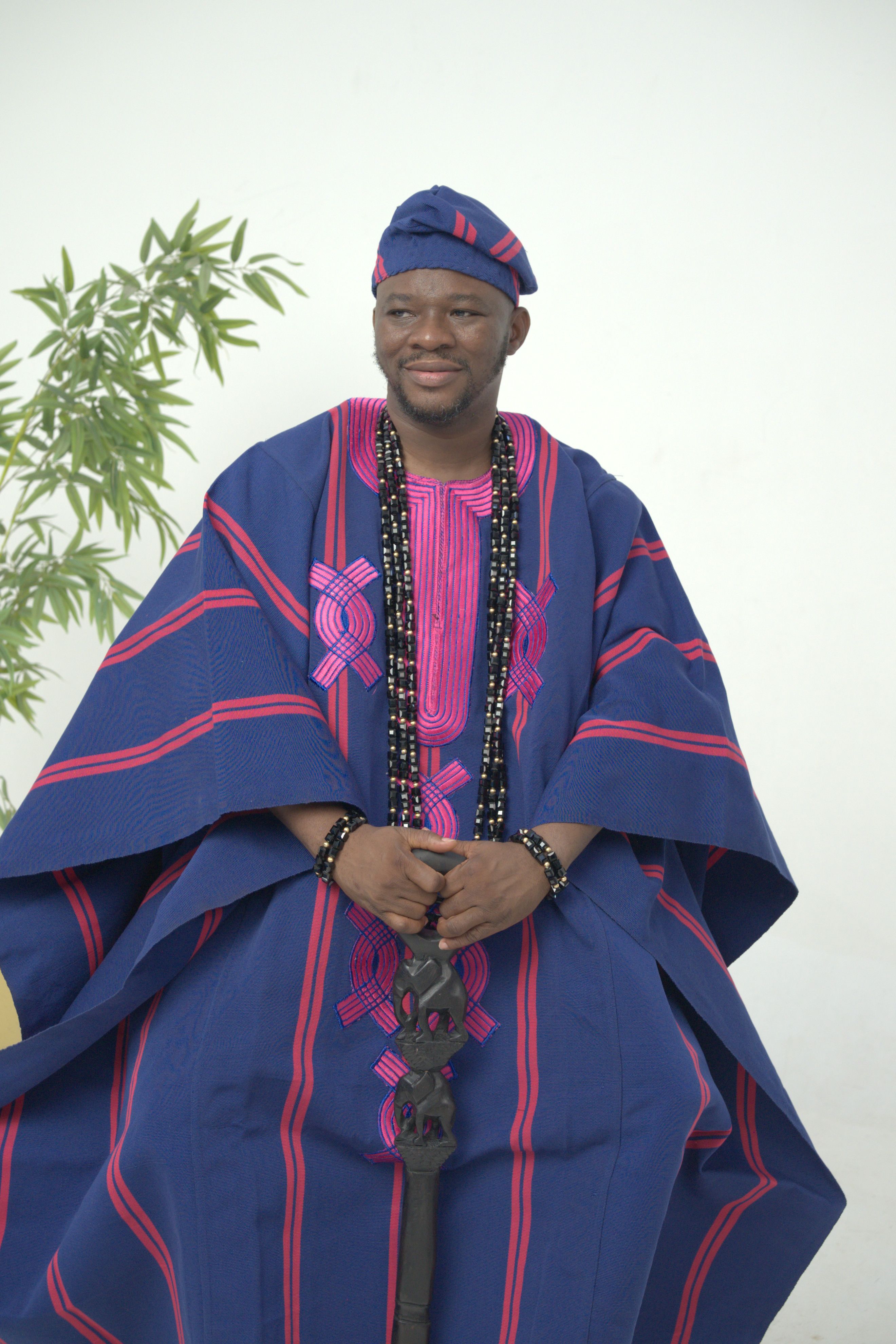 A Nigerian man wearing traditional Yoruba attire with vibrant colors indoors.