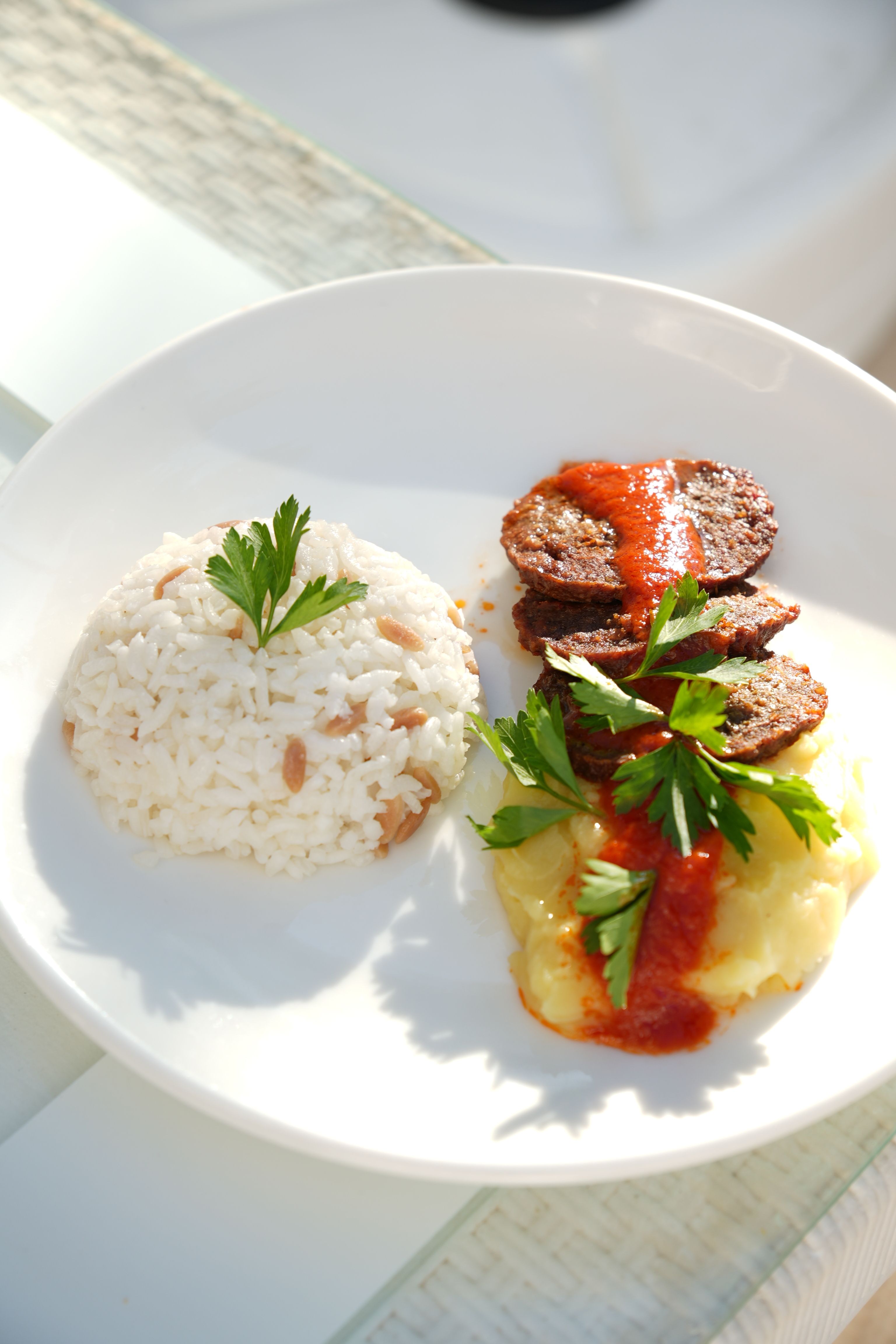 Tasty sausage with rice and mashed potatoes garnished with parsley on a white plate.
