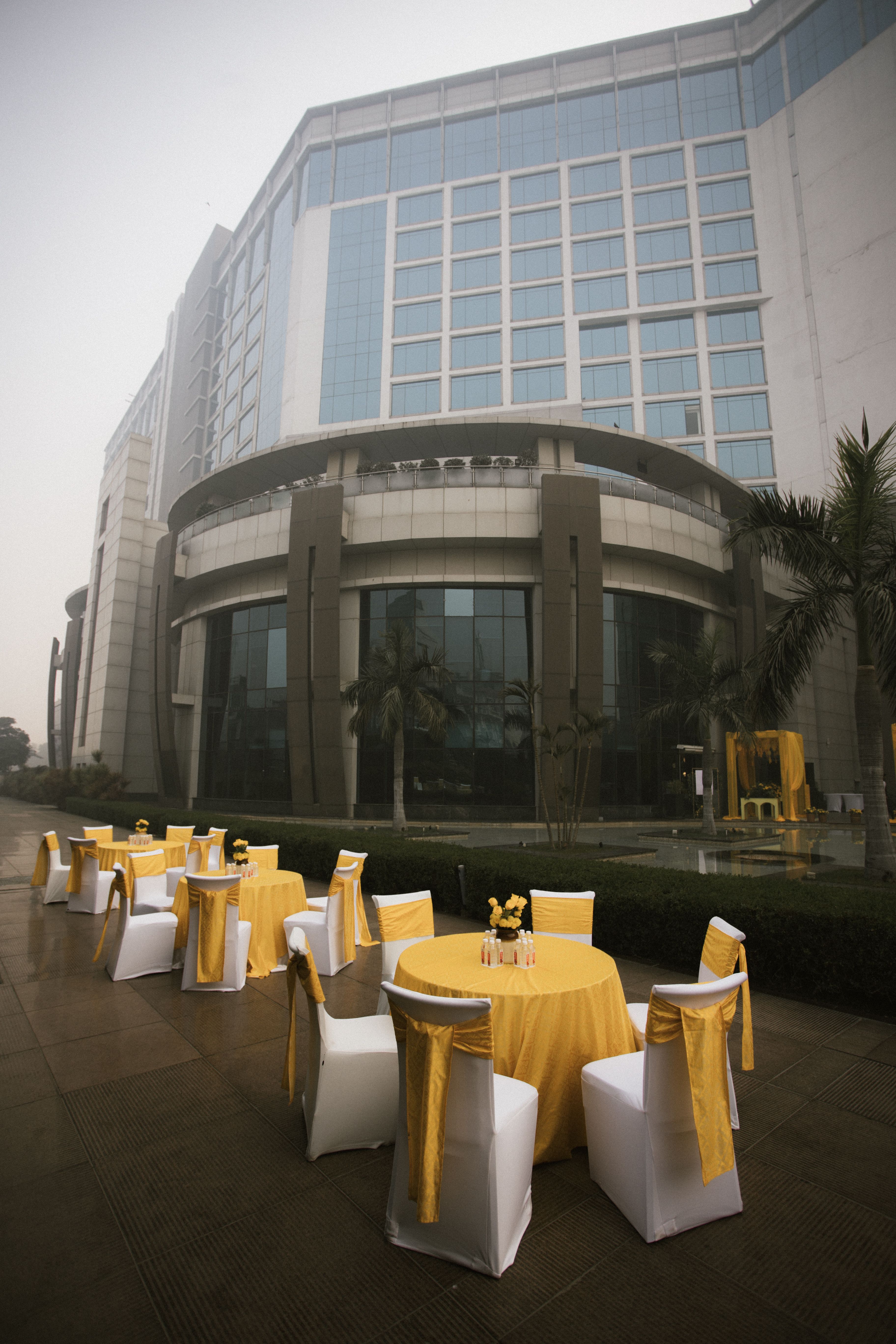 Circular tables with yellow covers arranged outdoors near a modern hotel building.