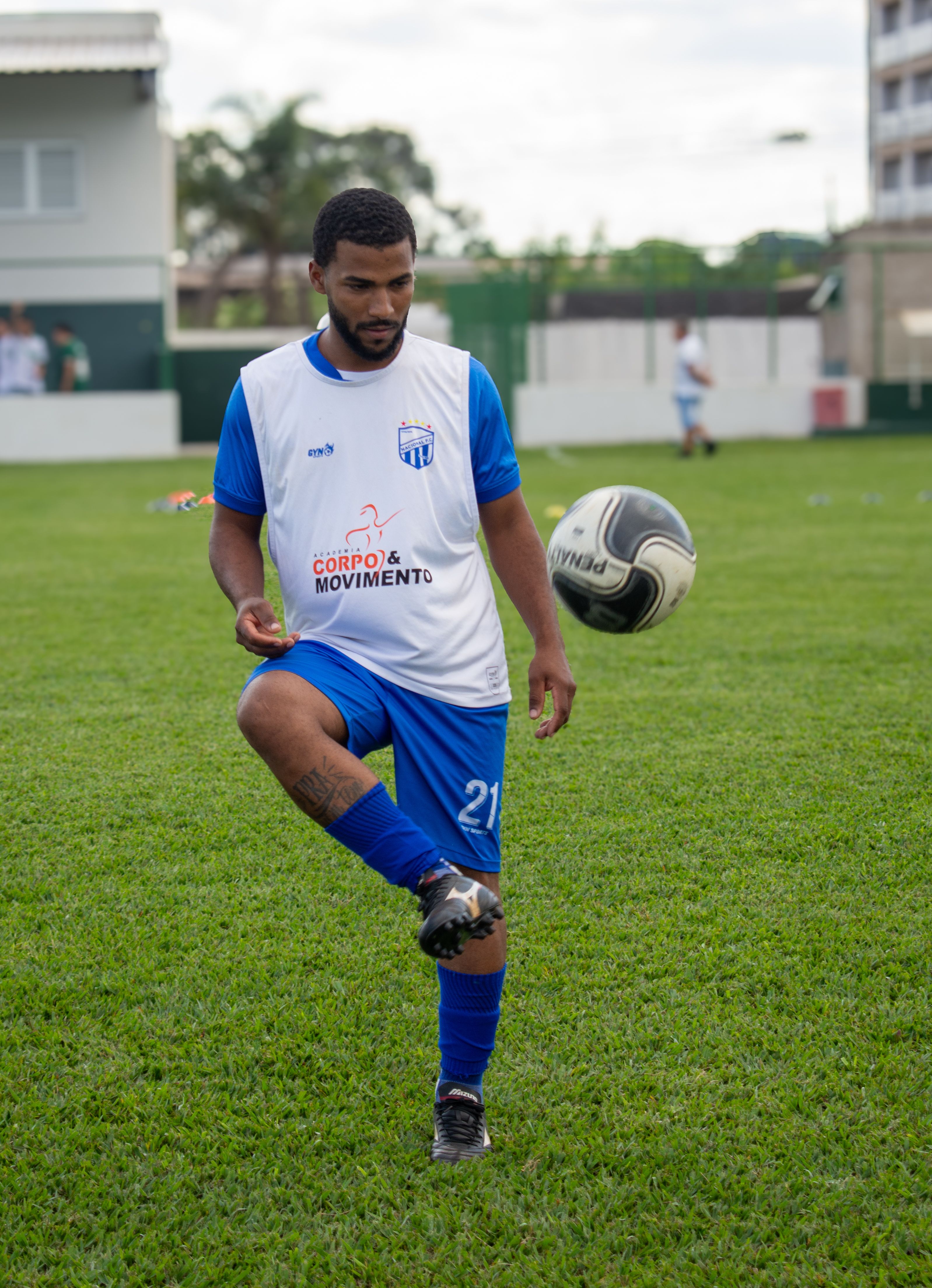 A male soccer player practicing ball control on a grassy field during the day.