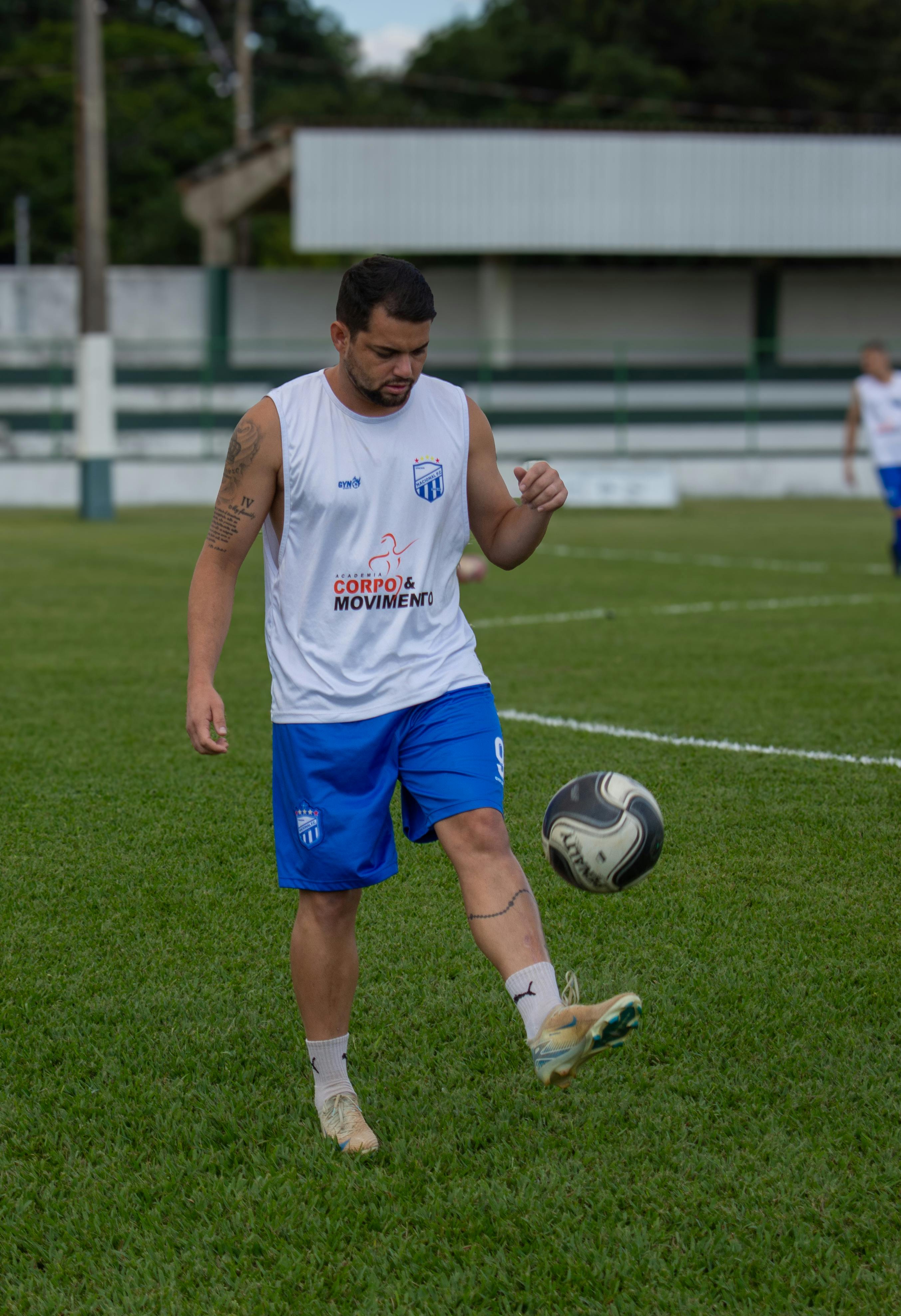 Male soccer player in white and blue uniform practicing outdoors on grass field.