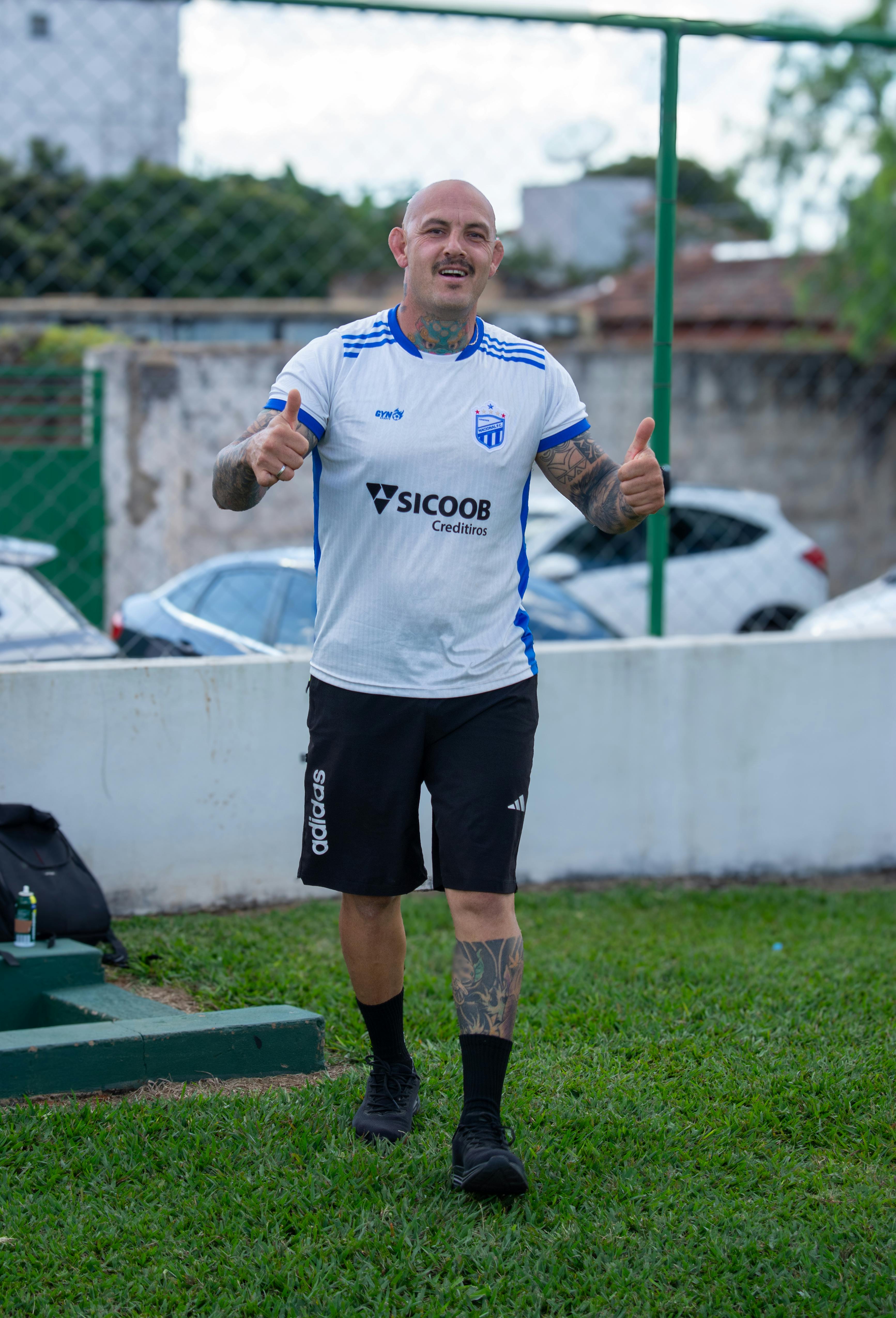 Bald man in sportswear giving thumbs up at a local football field.