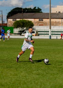 Soccer player dribbling the ball on a grass field during a daytime match with other players in the background.