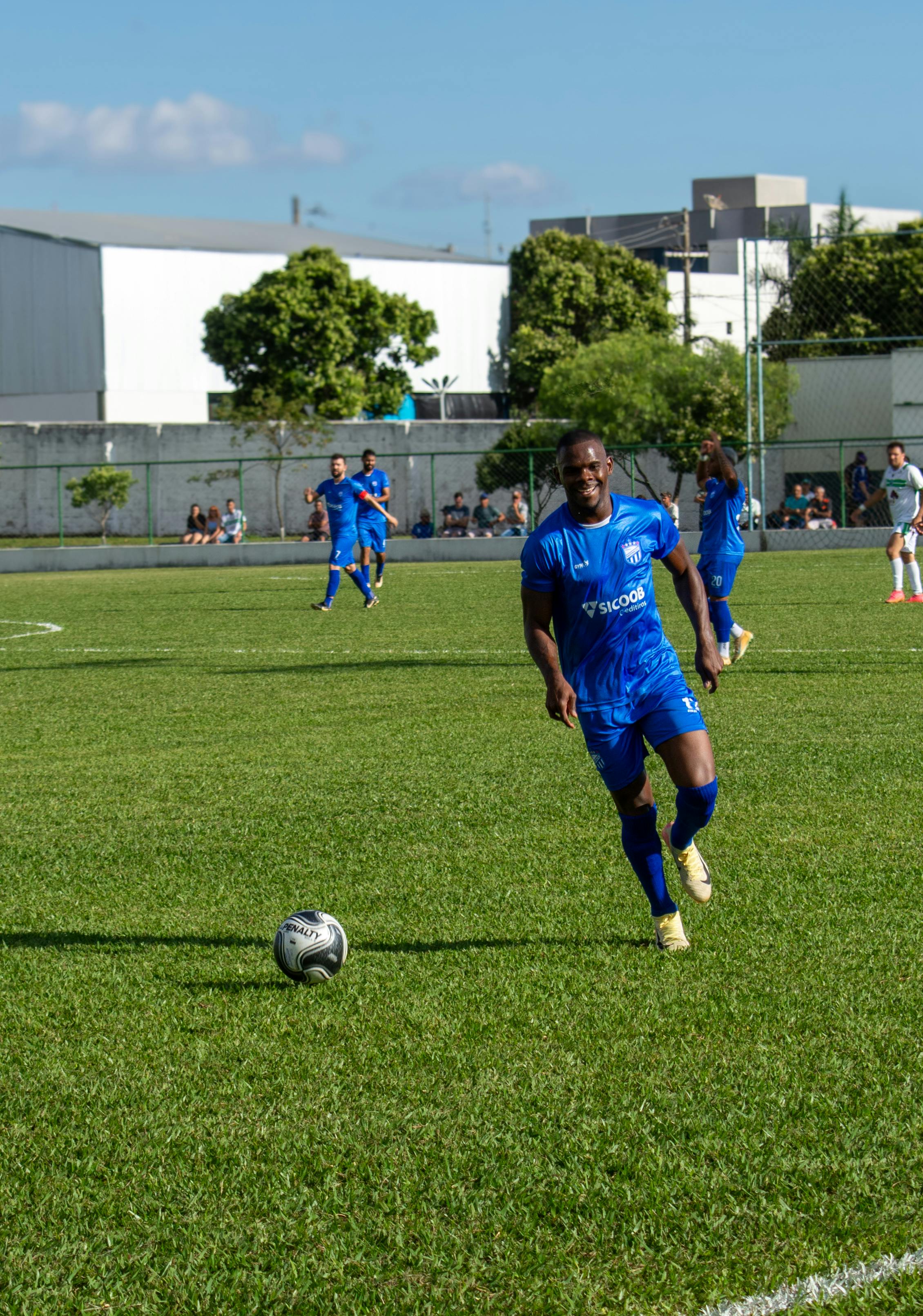 Action shot of soccer player in blue uniform during a daytime match on a grass field.