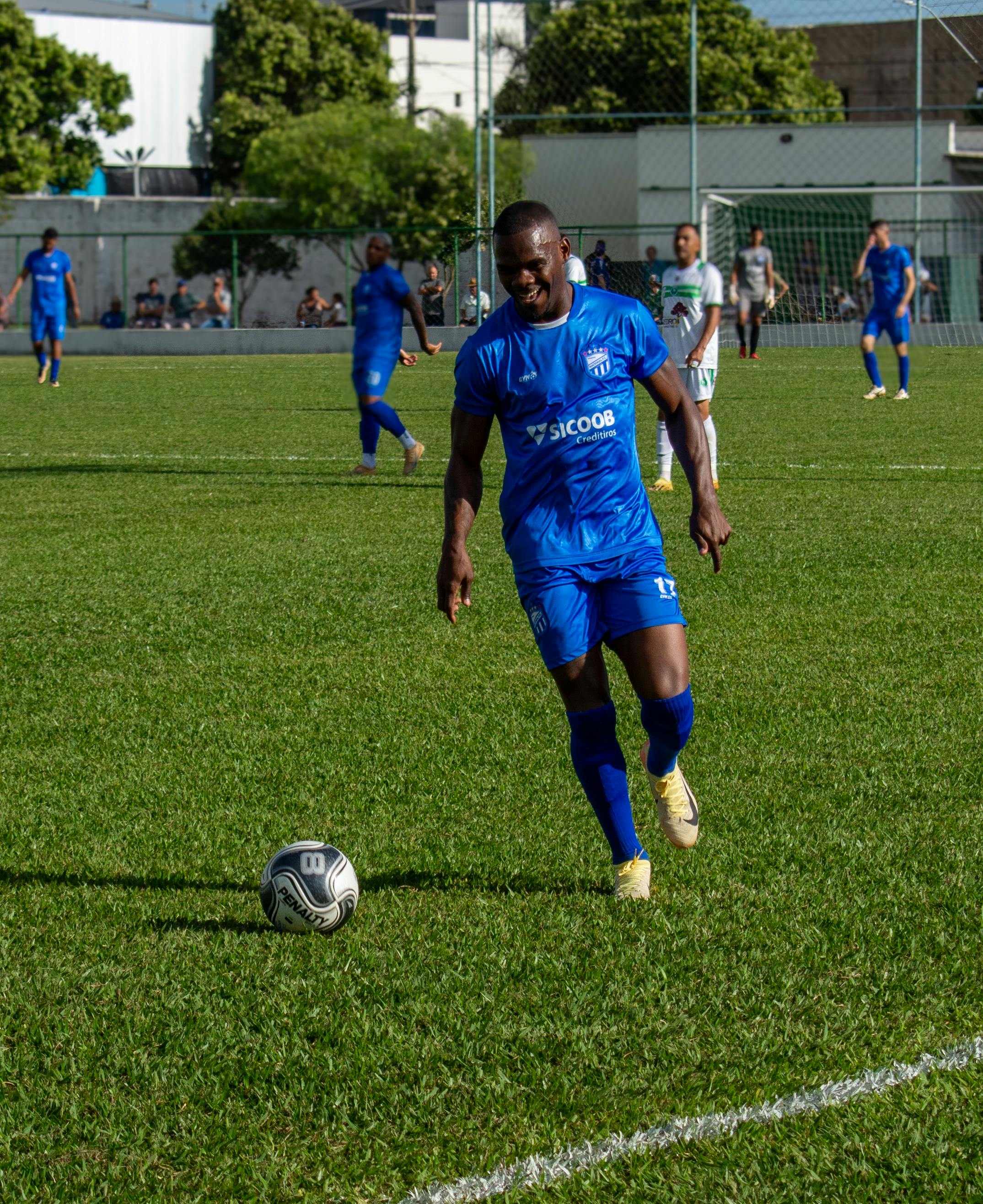 Action shot of a soccer game with a player dribbling a ball on a sunny day.