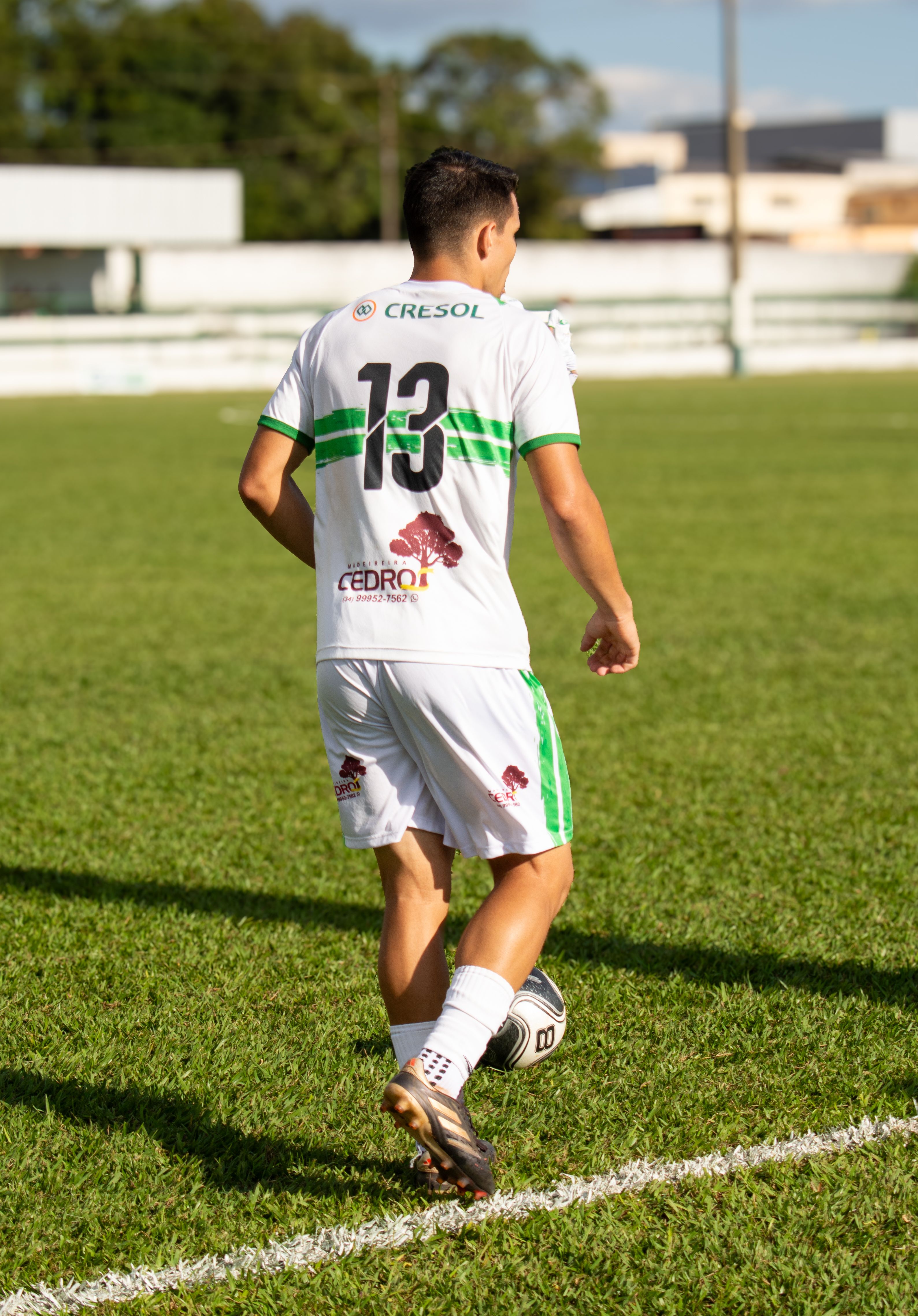 A soccer player dribbling the ball on a sunny day with green grass and a white uniform.