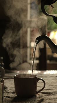 Cozy indoor scene with steam rising as hot tea is poured into a mug.