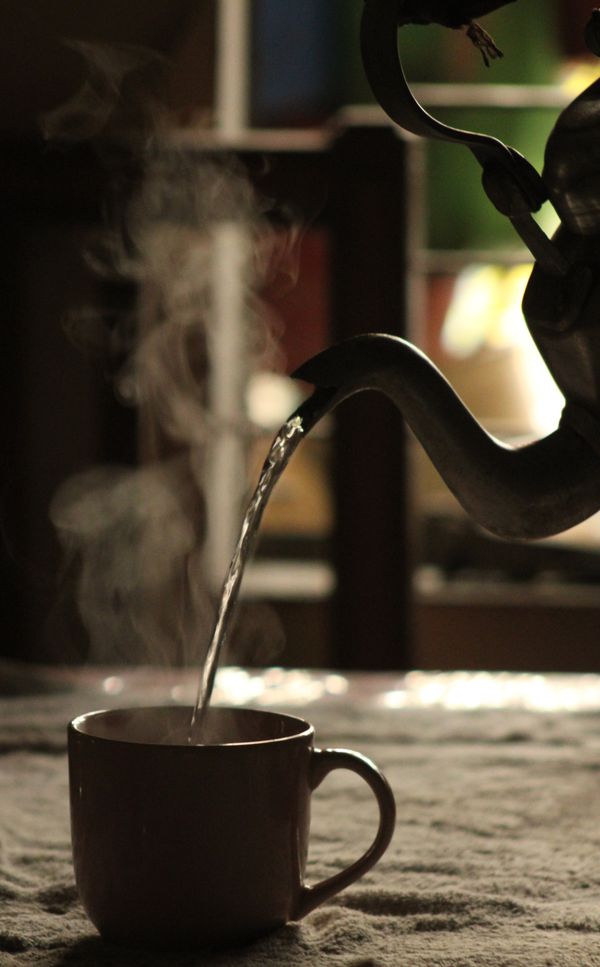 Hot tea being poured from a kettle into a mug