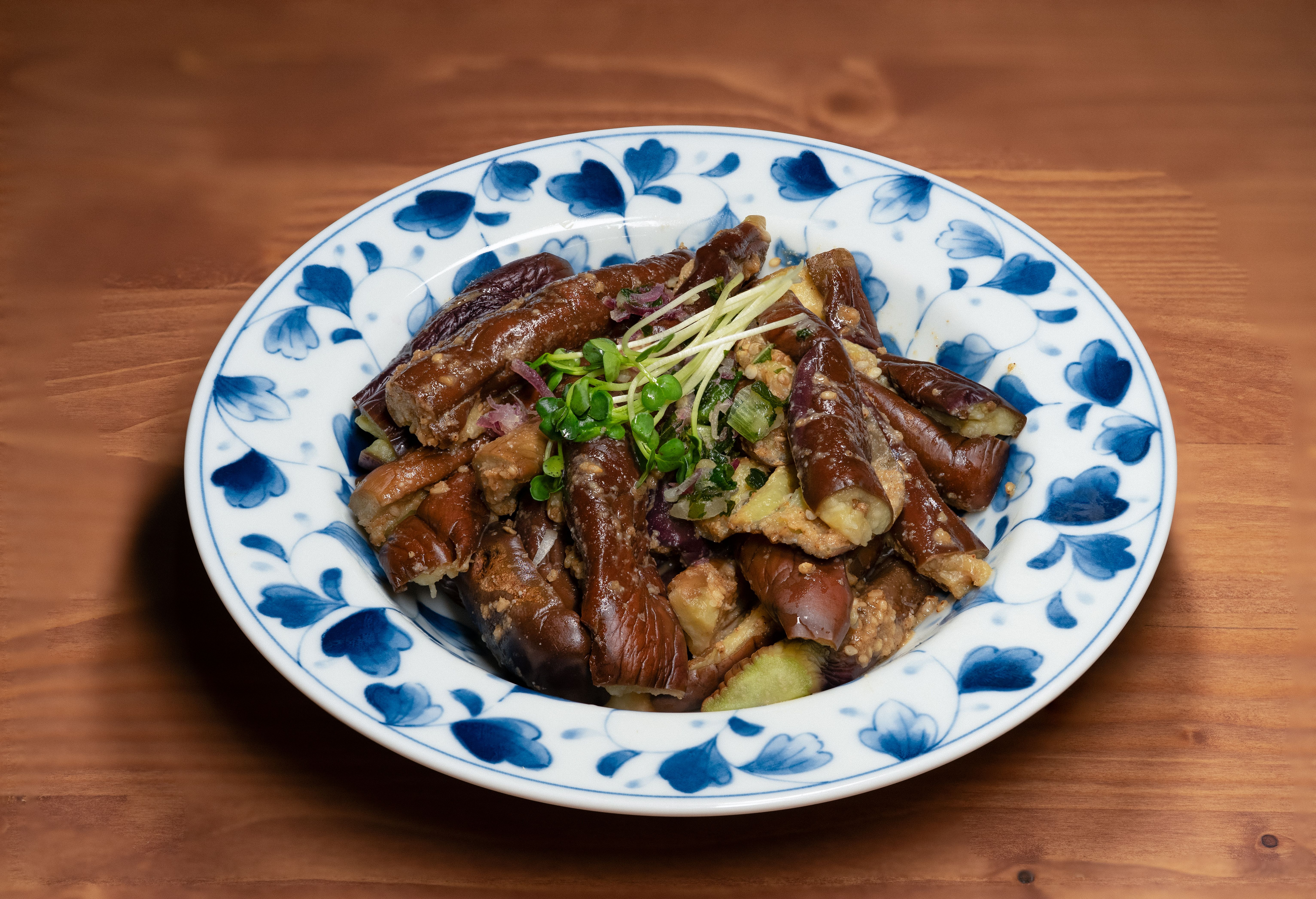 Golden chunks of Japanese eggplant glazed in a rich, glossy reddish-brown miso sauce, garnished with bright green scallion slices in a dark ceramic bowl over steamed white rice