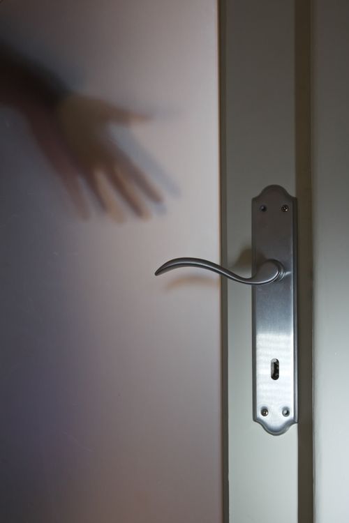 Free A mysterious shadow of a hand reaching behind a frosted glass door with a metallic handle. Stock Photo