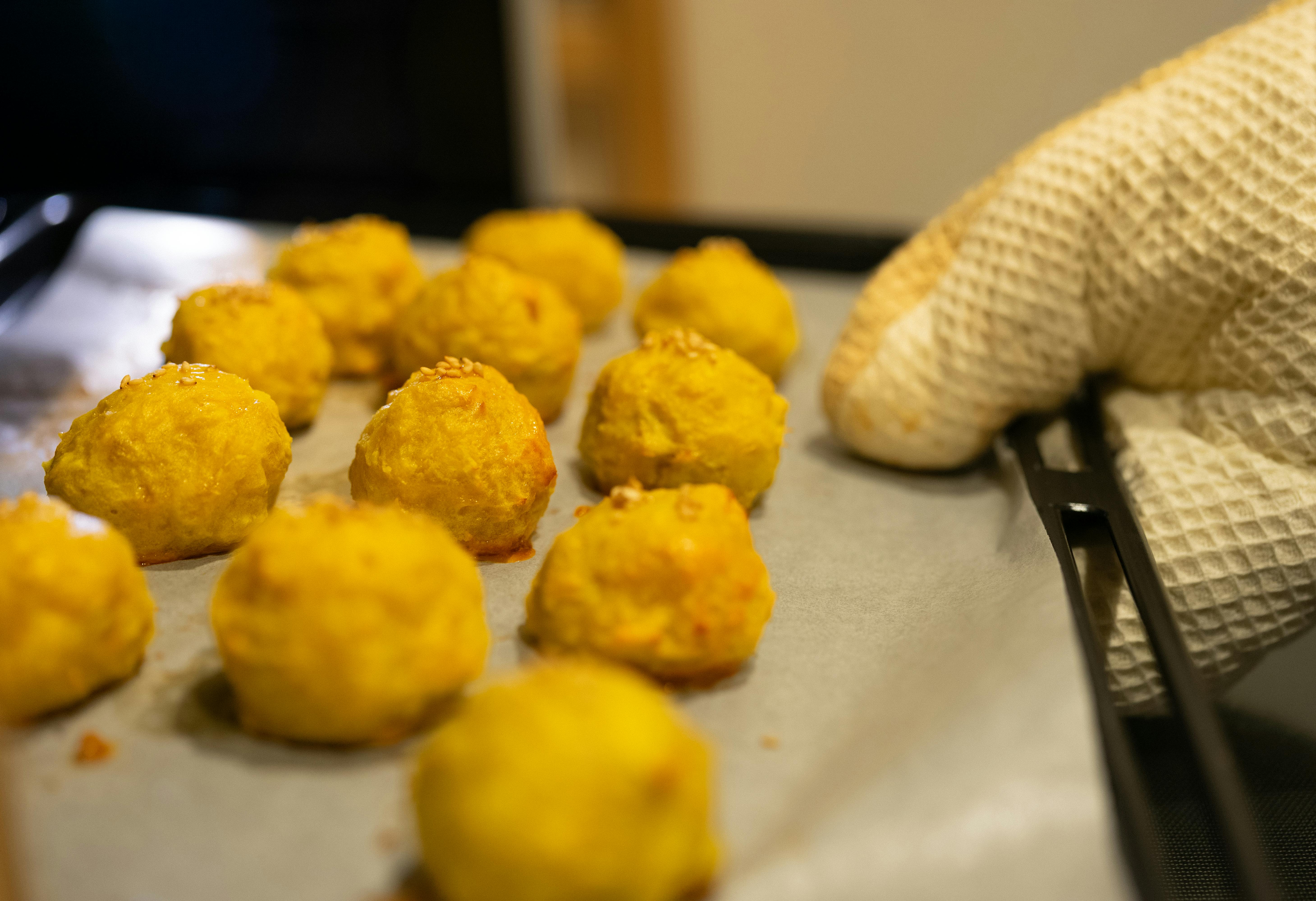 Gloved hand removing a tray of freshly baked golden cheese balls from the oven.