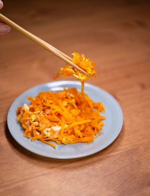 Free Close-up of shredded carrot salad with egg being picked up by chopsticks on a wooden table. Stock Photo