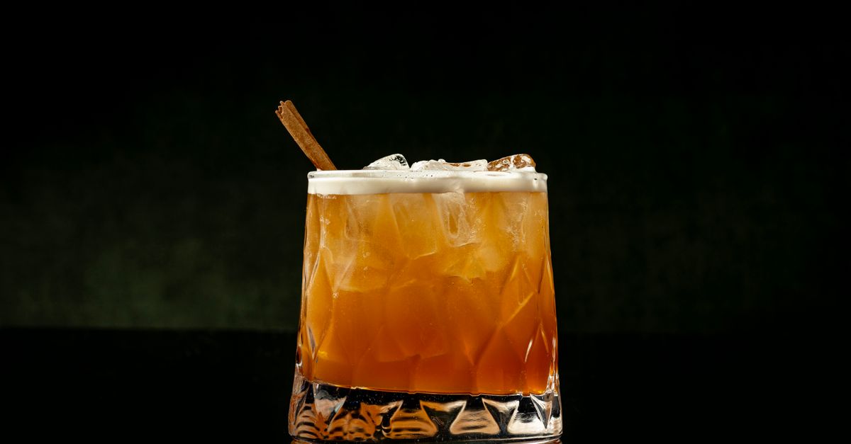 Classic whiskey cocktail with ice and cinnamon stick on a moody background.
