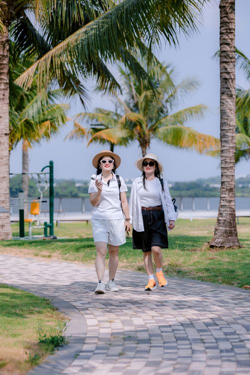 Free Two women enjoying a sunny walk on a palm-lined pathway near a body of water. Stock Photo