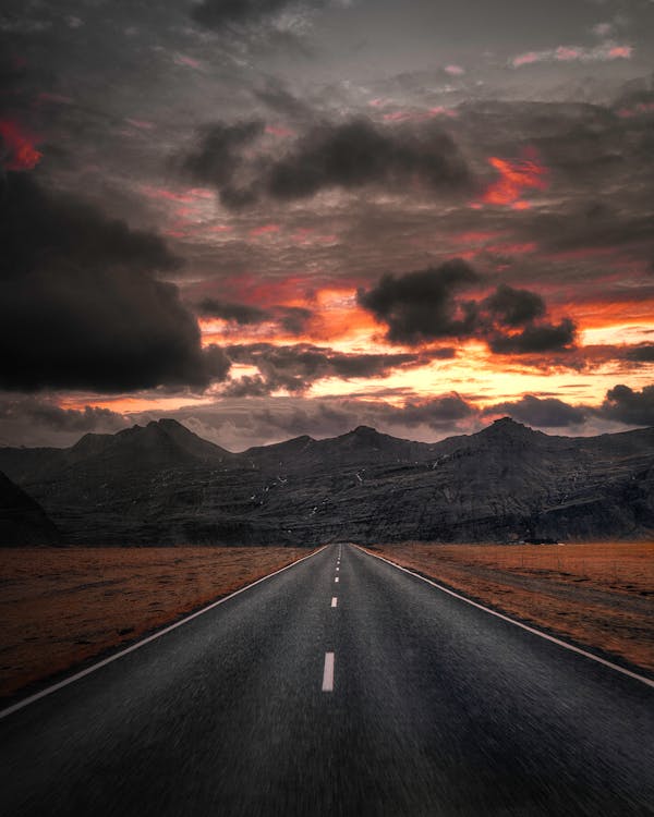 Black Asphalt Road Near Mountains Under Cloudy Sky