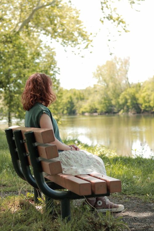 Free Woman enjoys tranquil river scene from a park bench in spring. Stock Photo