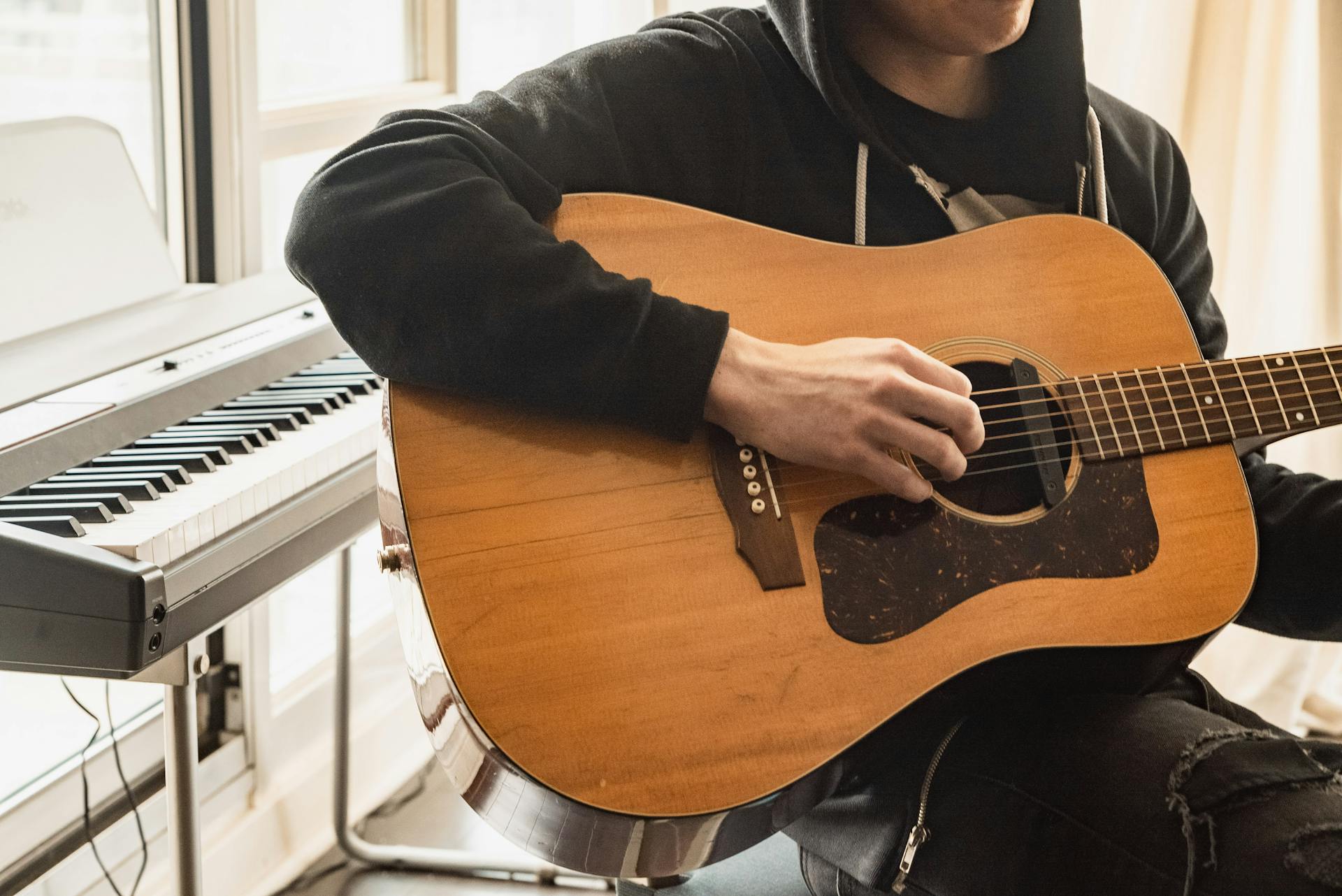 A musician playing an acoustic guitar next to a digital keyboard in a cozy indoor setting.