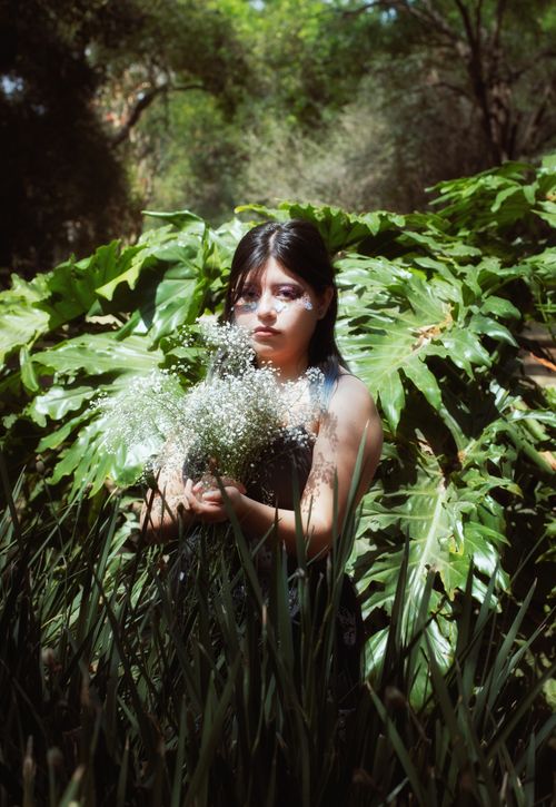 Free A woman holds a bouquet amidst a lush jungle backdrop in bright daylight, capturing a moment of natural beauty. Stock Photo