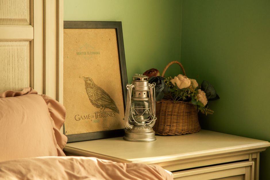 Warmly lit bedroom corner with poster, lantern, and floral basket adding vintage charm.