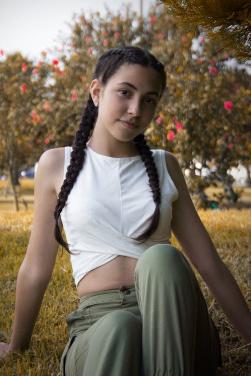 Woman in White Tank Top and Gray Pants Sitting on Green Grass Field