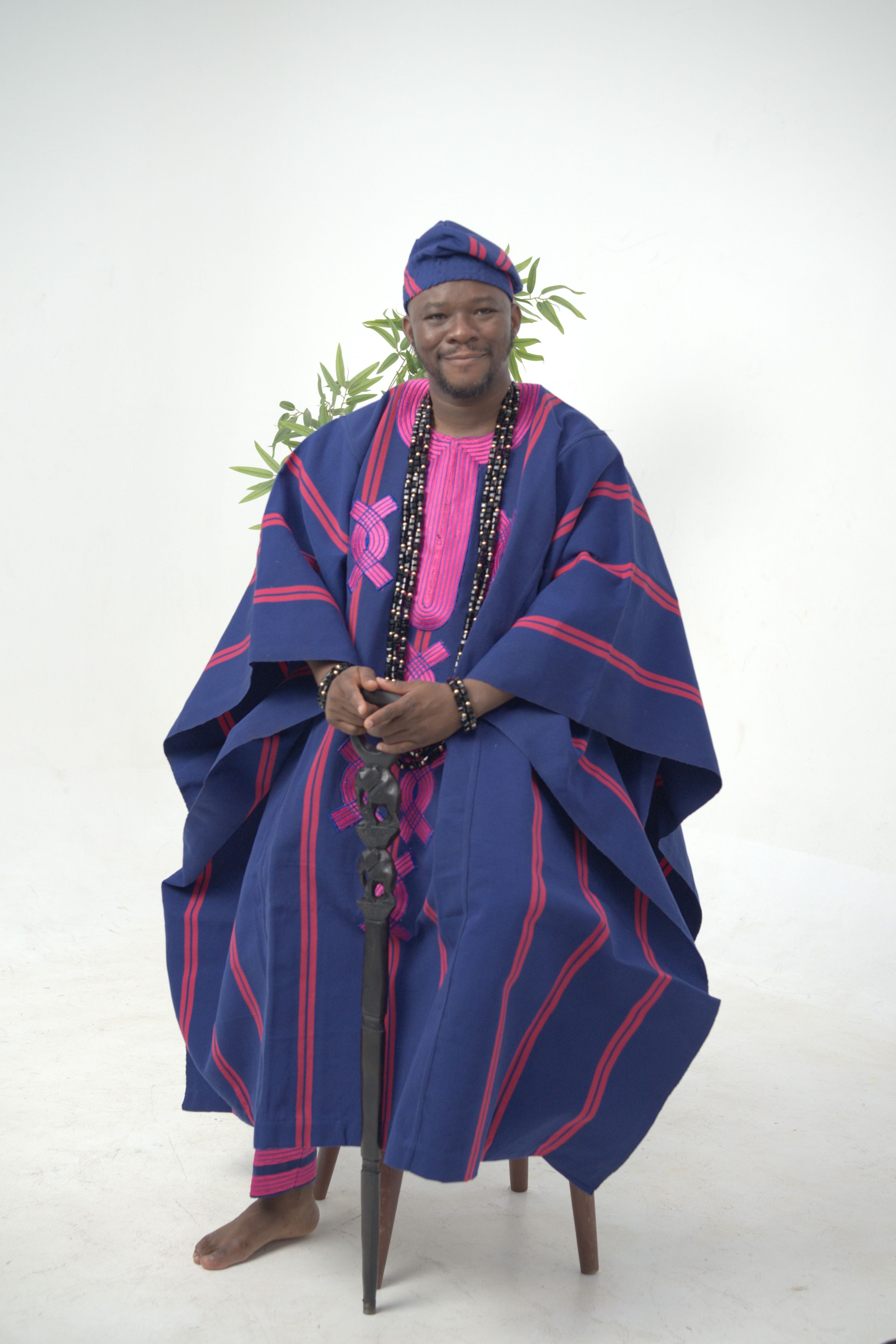African man wearing traditional agbada attire sitting indoors.