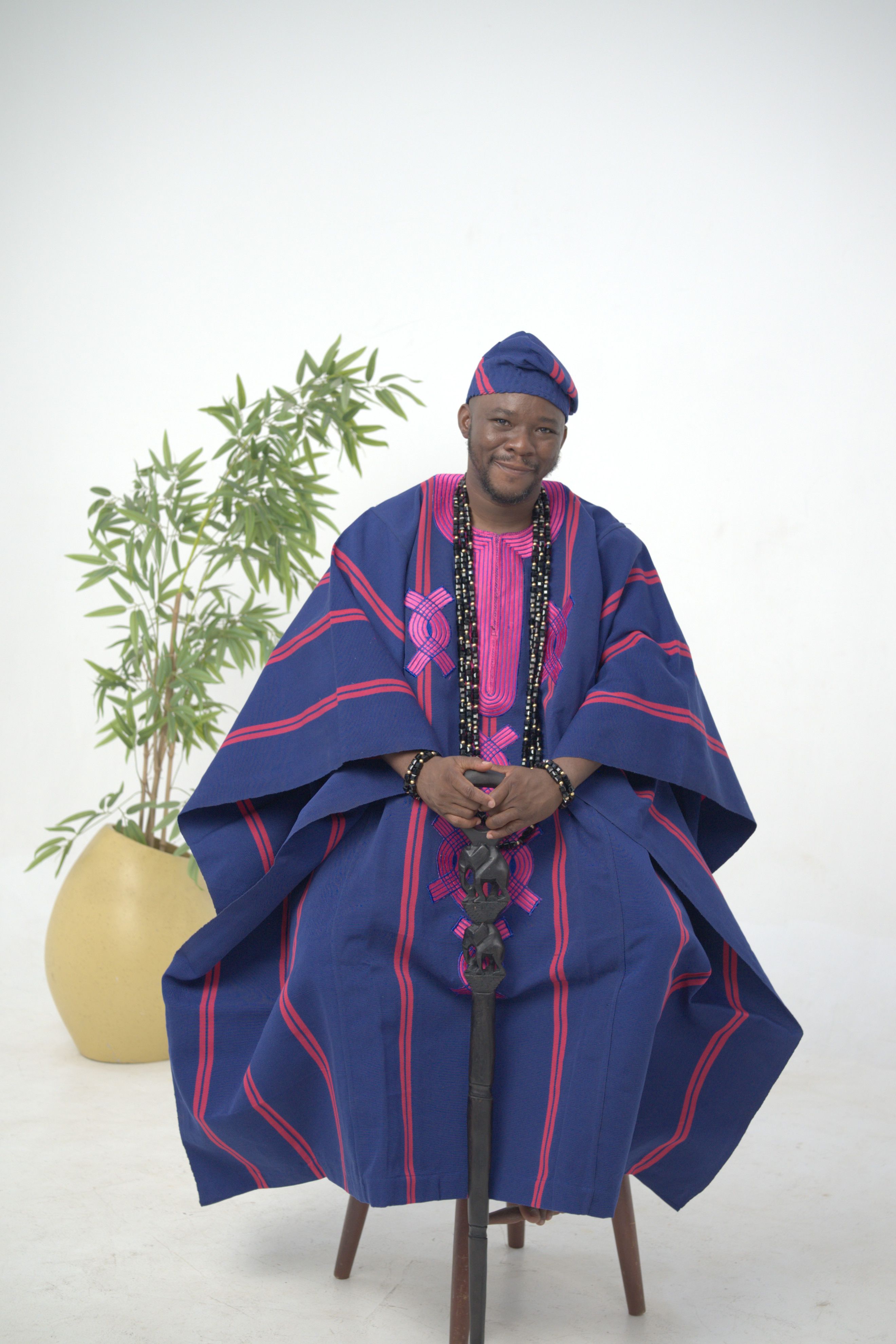 Portrait of a man in traditional Nigerian attire with plant in background.