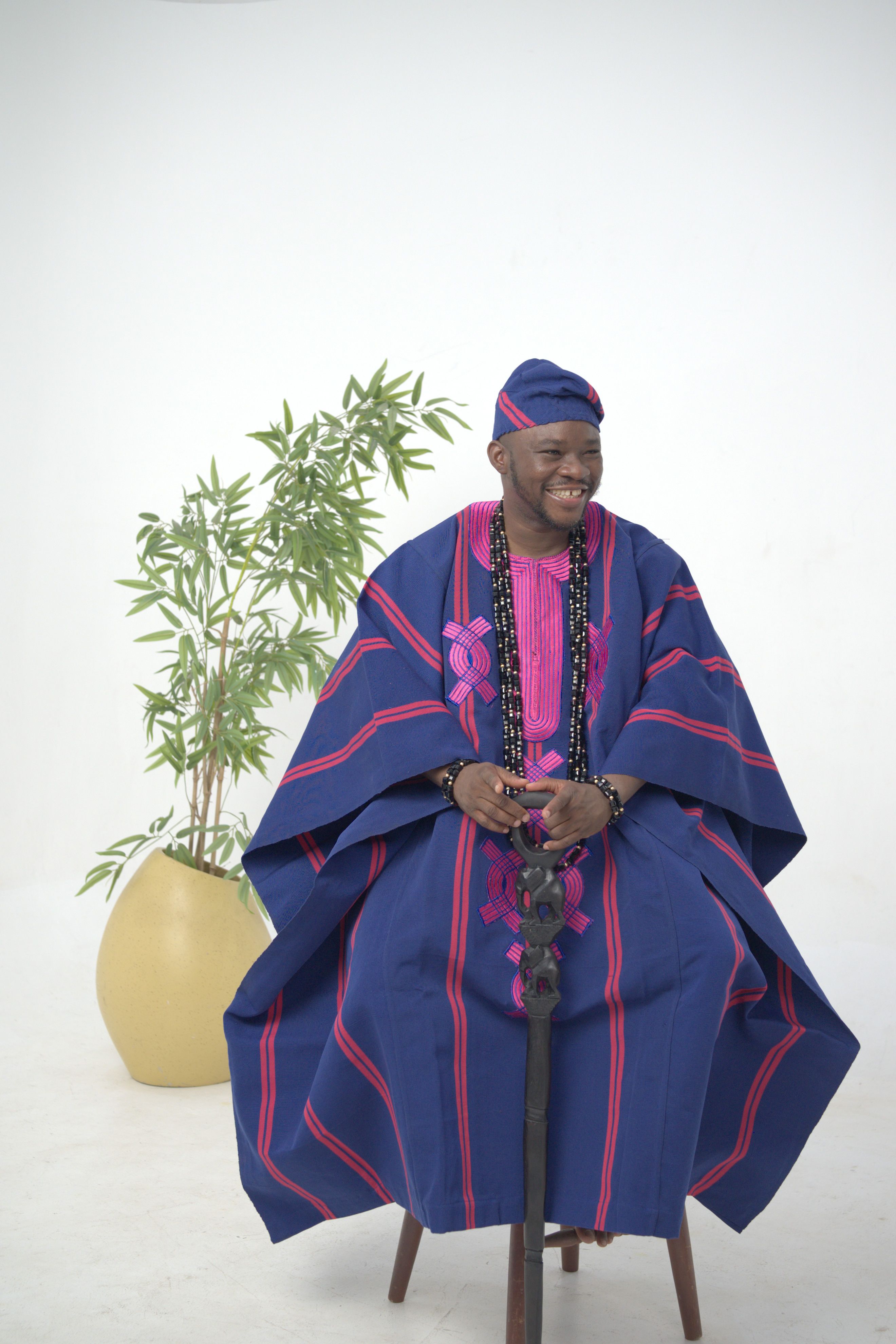 Portrait of an adult Nigerian man wearing blue and pink agbada, sitting indoors.