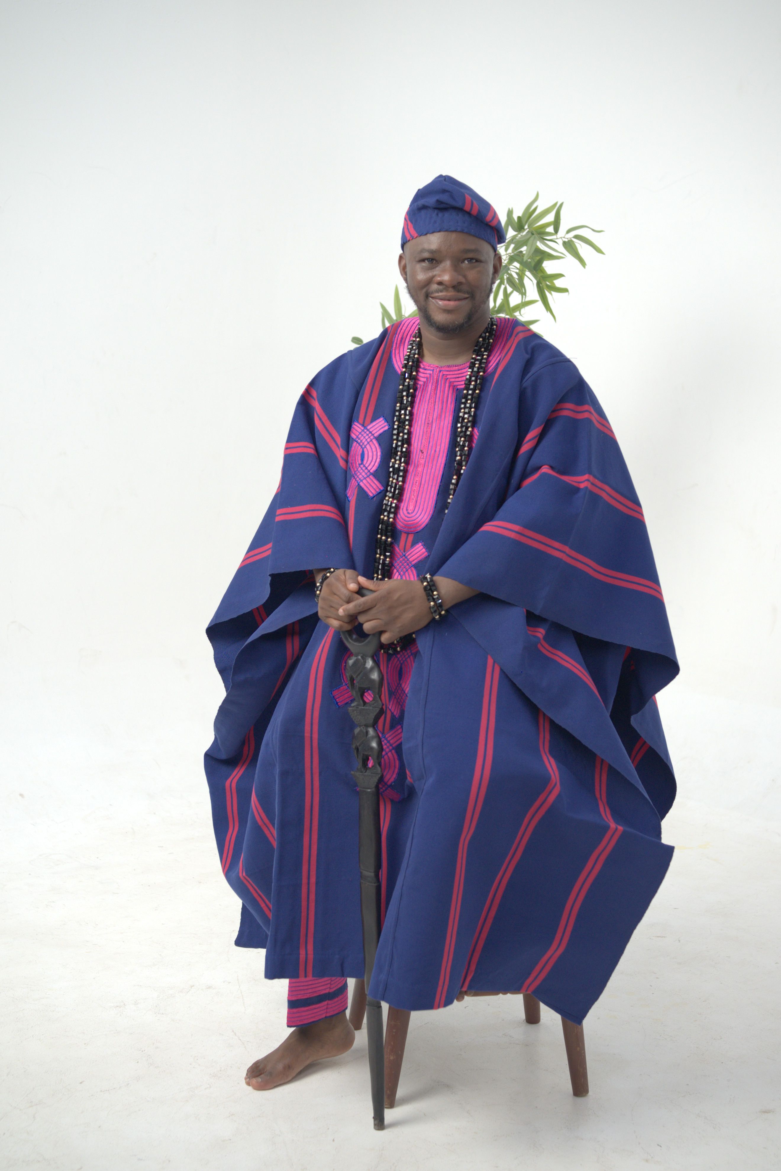 Portrait of a man in traditional Nigerian agbada attire sitting indoors with a confident smile.