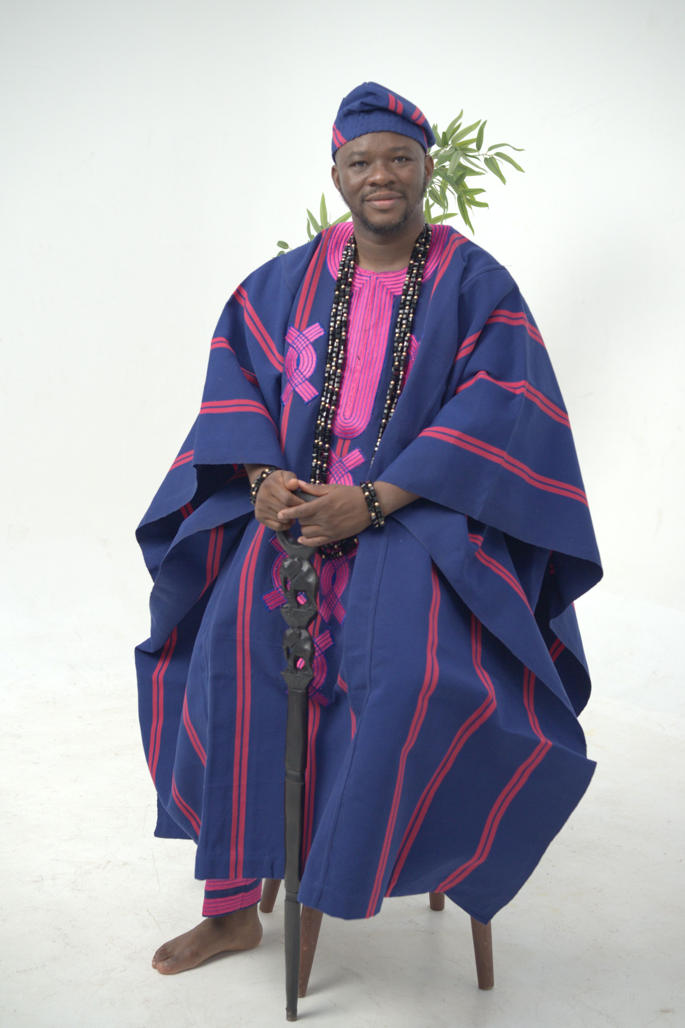 Man wearing traditional Nigerian agbada, seated and smiling against a neutral backdrop.