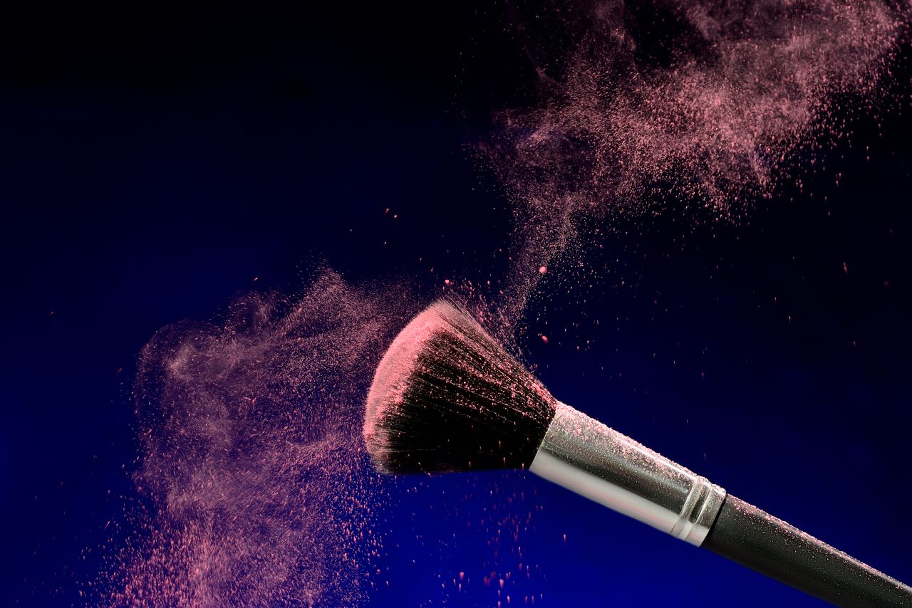 pink powder swirls around a makeup brush against a dark background sho