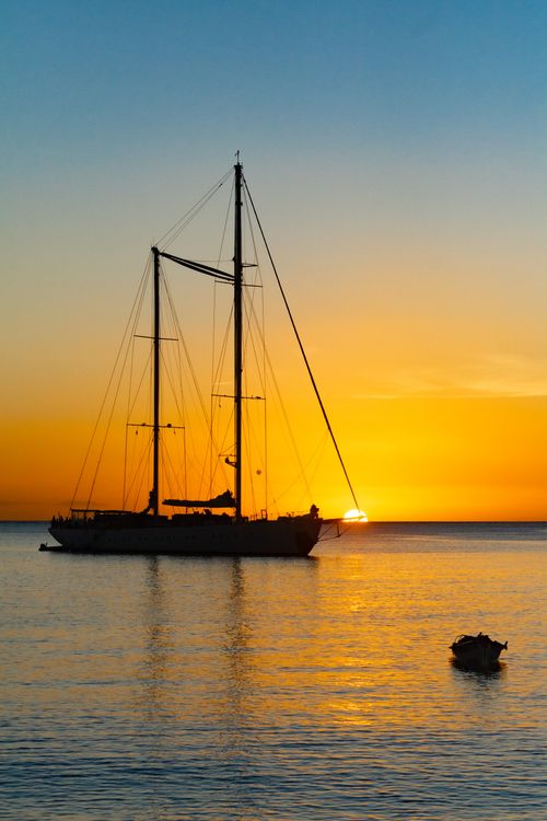 Free A serene sunset view with a sailboat silhouette on a calm sea, perfect for travel themes. Stock Photo