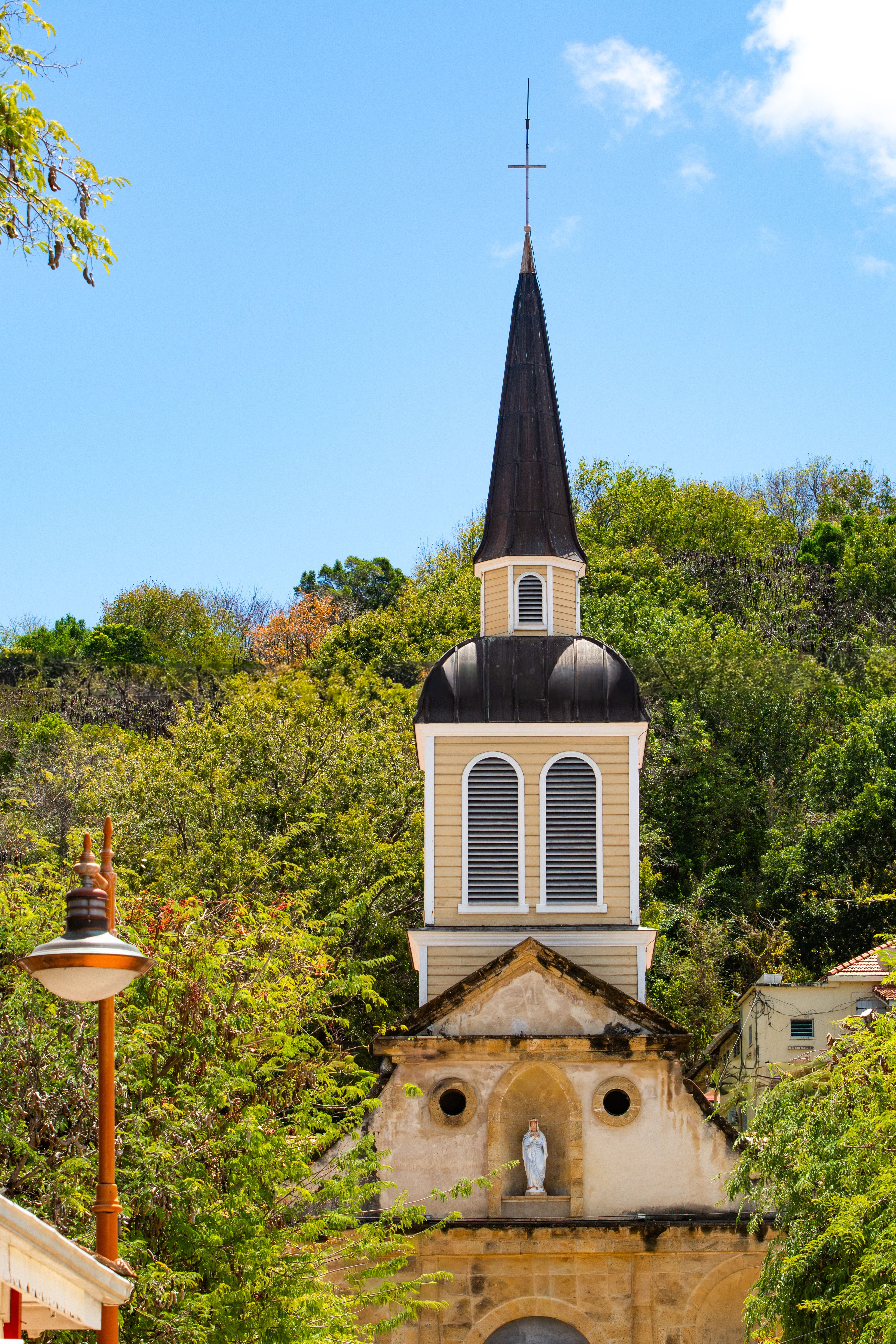 A picturesque colonial church tower surrounded by lush greenery under a clear blue sky.