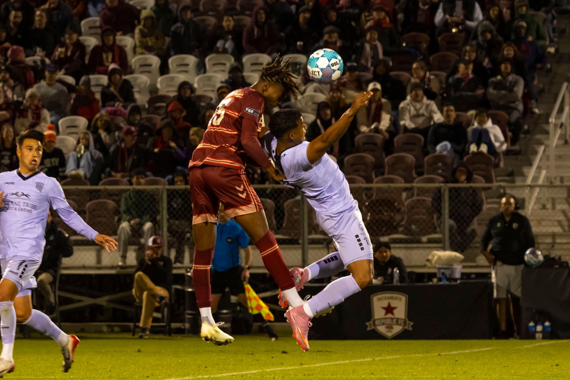 MLS players contesting a midfield duel on a packed American stadium pitch under clear evening skies