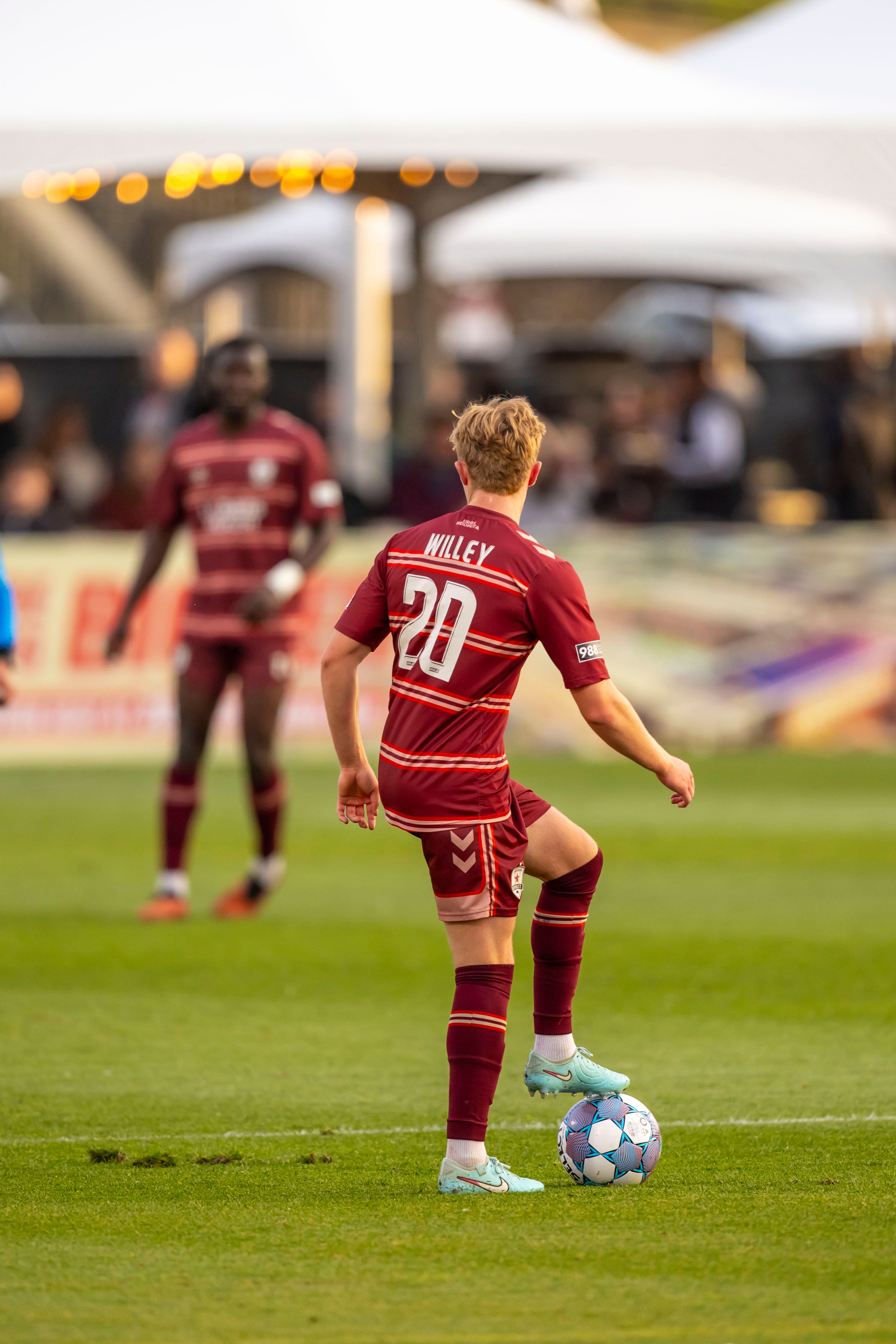 A soccer player prepares to kick the ball during a match, wearing a red uniform on a green field.