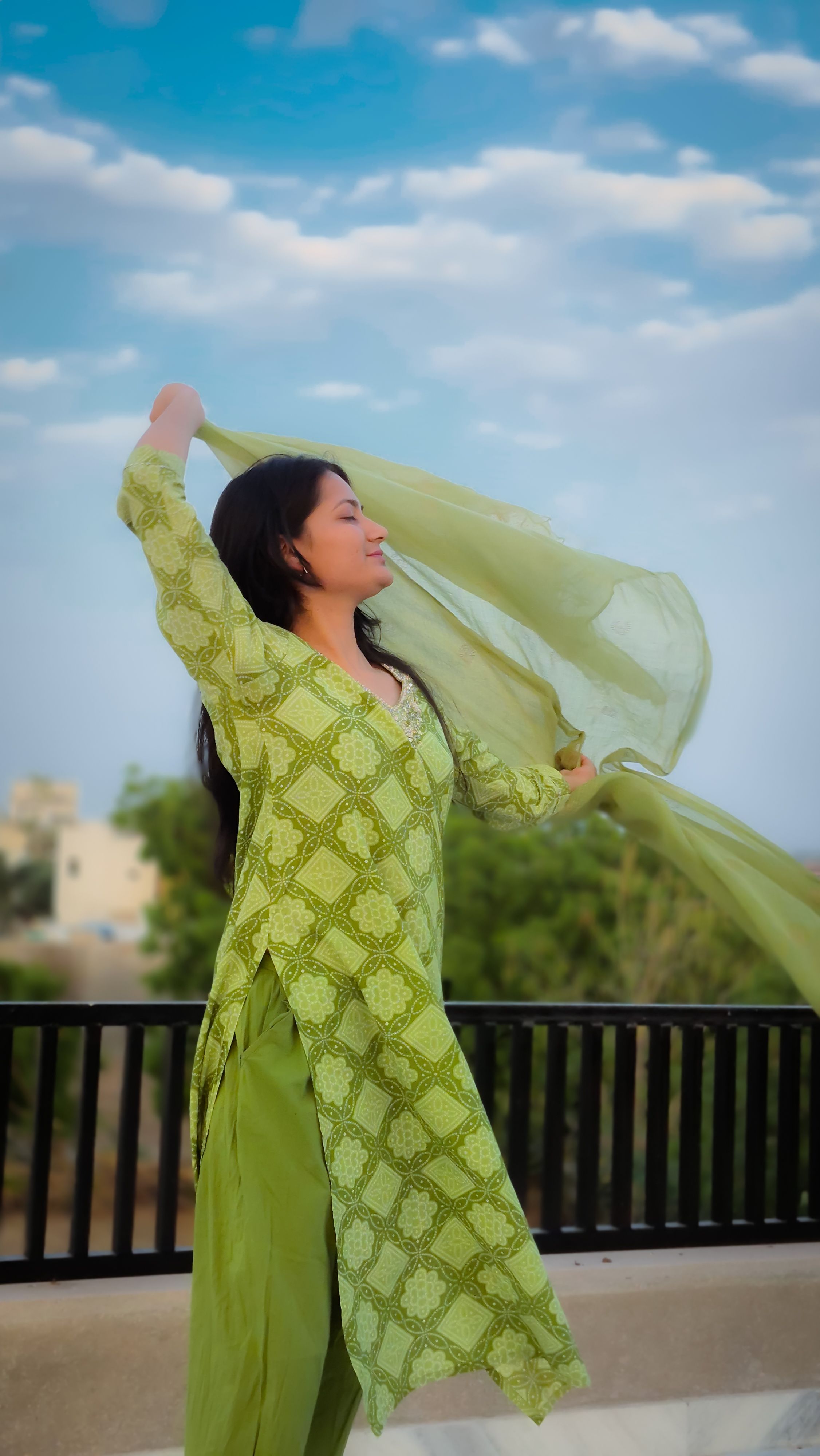 South Asian woman in green attire enjoying a breezy day outdoors, filled with energy and confidence.
