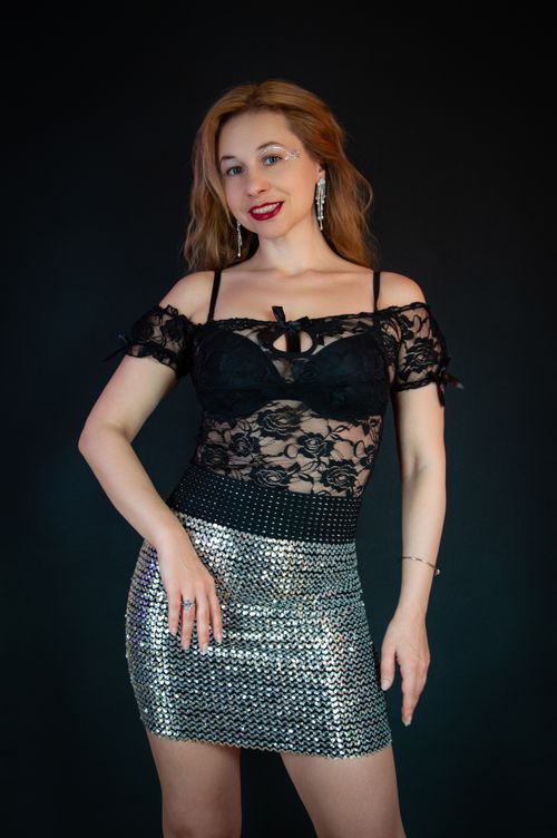 Free A stylish woman in a black lace top and silver skirt poses confidently against a dark background. Stock Photo