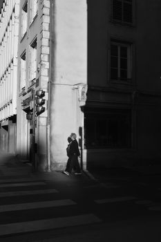 Black and white street photo with pedestrians amidst dramatic shadows.