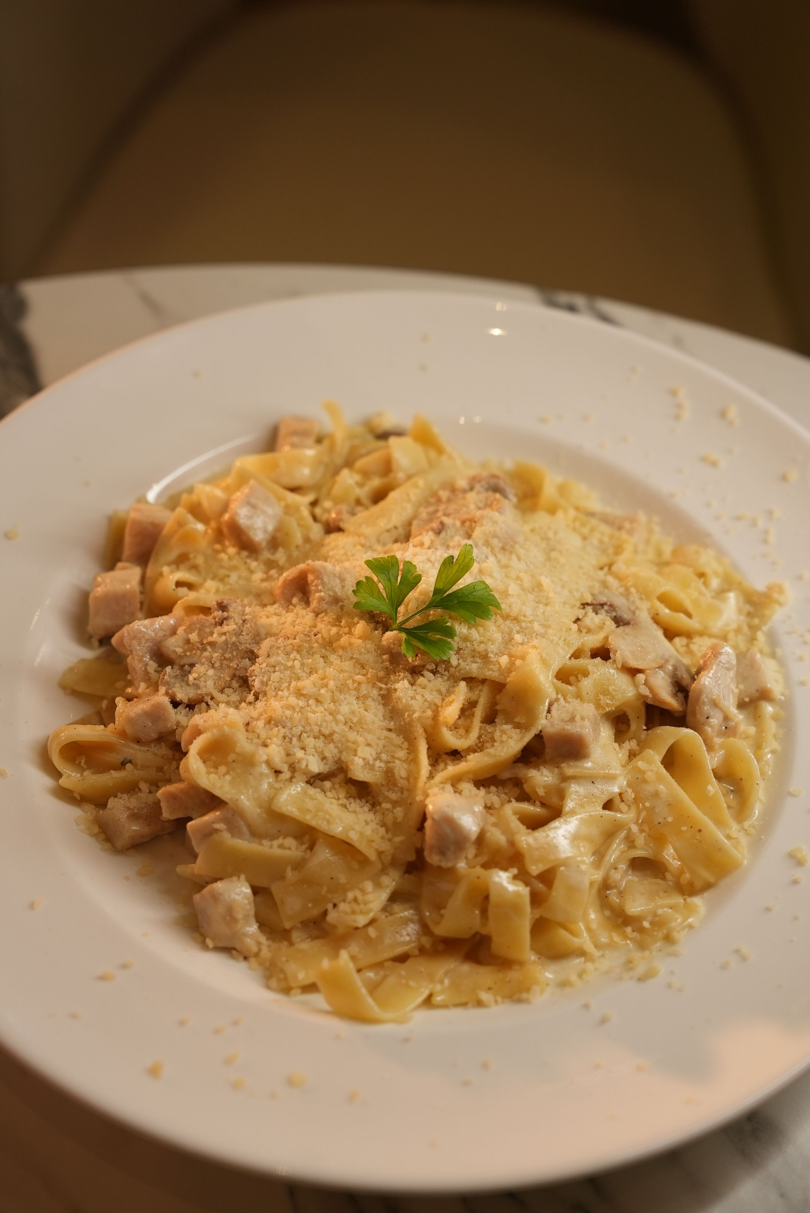 Tasty fettuccine alfredo with chicken and cheese on a white plate.