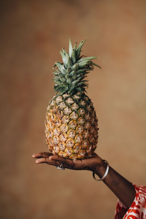 Free A hand gracefully holds a pineapple against a warm gradient backdrop, showcasing tropical fruit elegance. Stock Photo