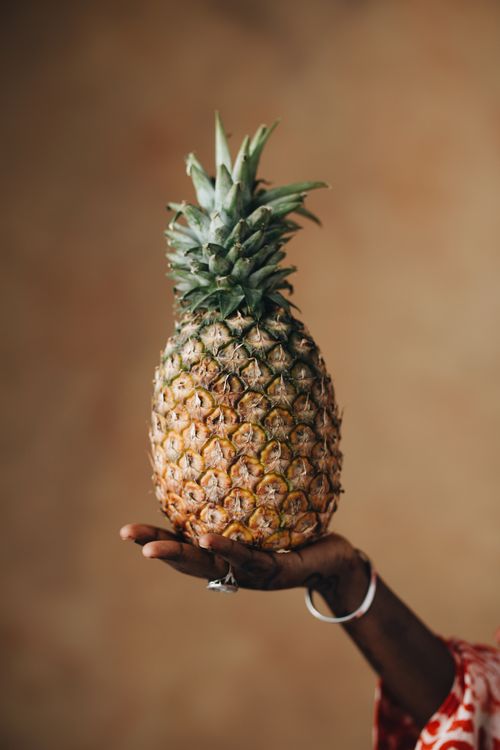 Free A fresh pineapple held up by a hand against a warm, earthy background. Perfect for food and lifestyle themes. Stock Photo