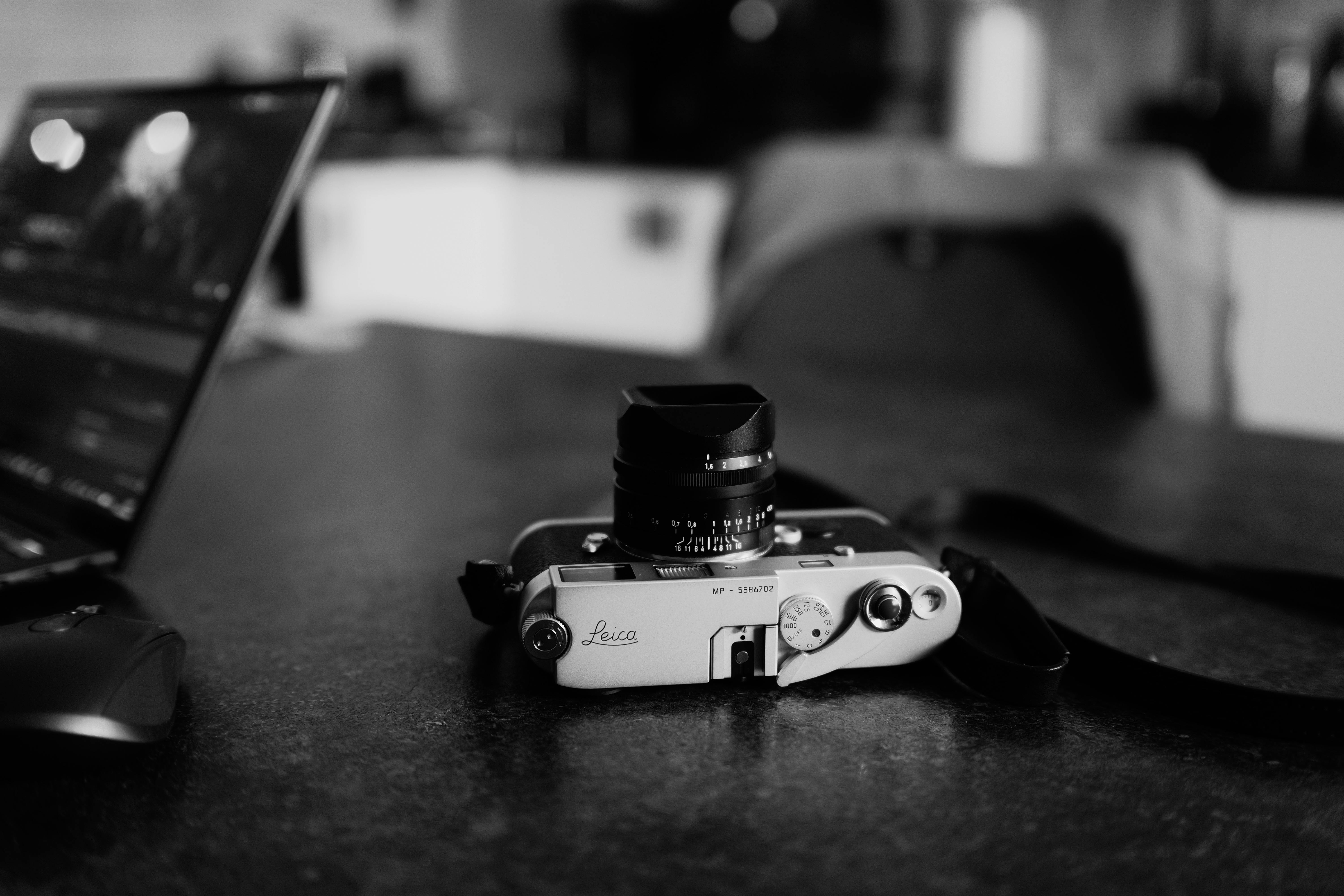 Monochrome image of a vintage camera and laptop on a desk, evoking a classic feel.