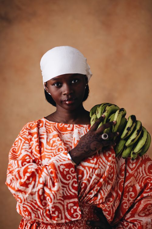 Free Portrait of a Nigerian woman in traditional attire holding a bunch of plantains, showcasing cultural heritage. Stock Photo