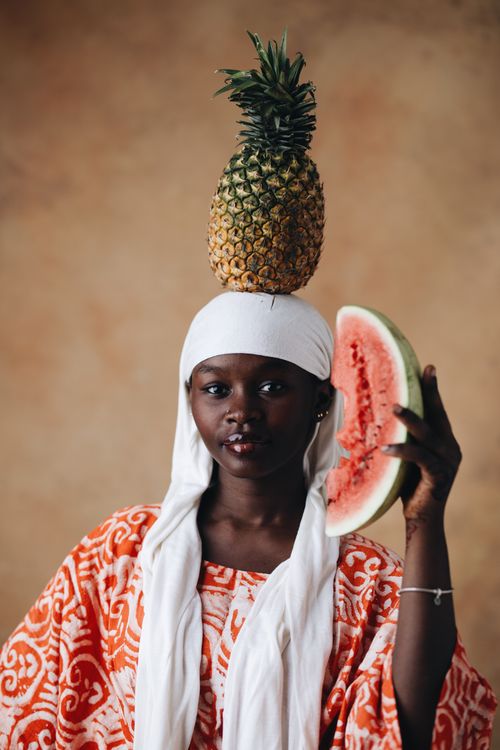 Free Artistic portrait of a woman balancing a pineapple and holding watermelon, embodying cultural expression. Stock Photo