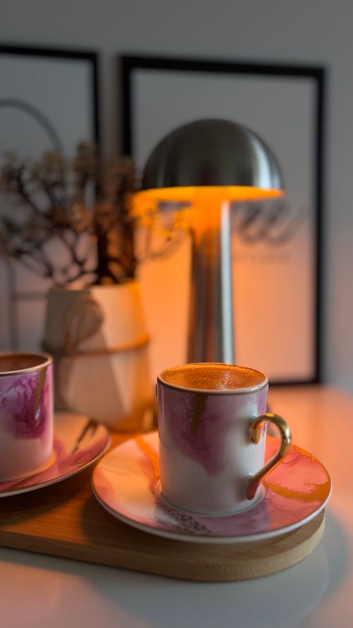 Free Elegant coffee cups on saucers under a warm lamp, creating a cozy indoor atmosphere. Stock Photo