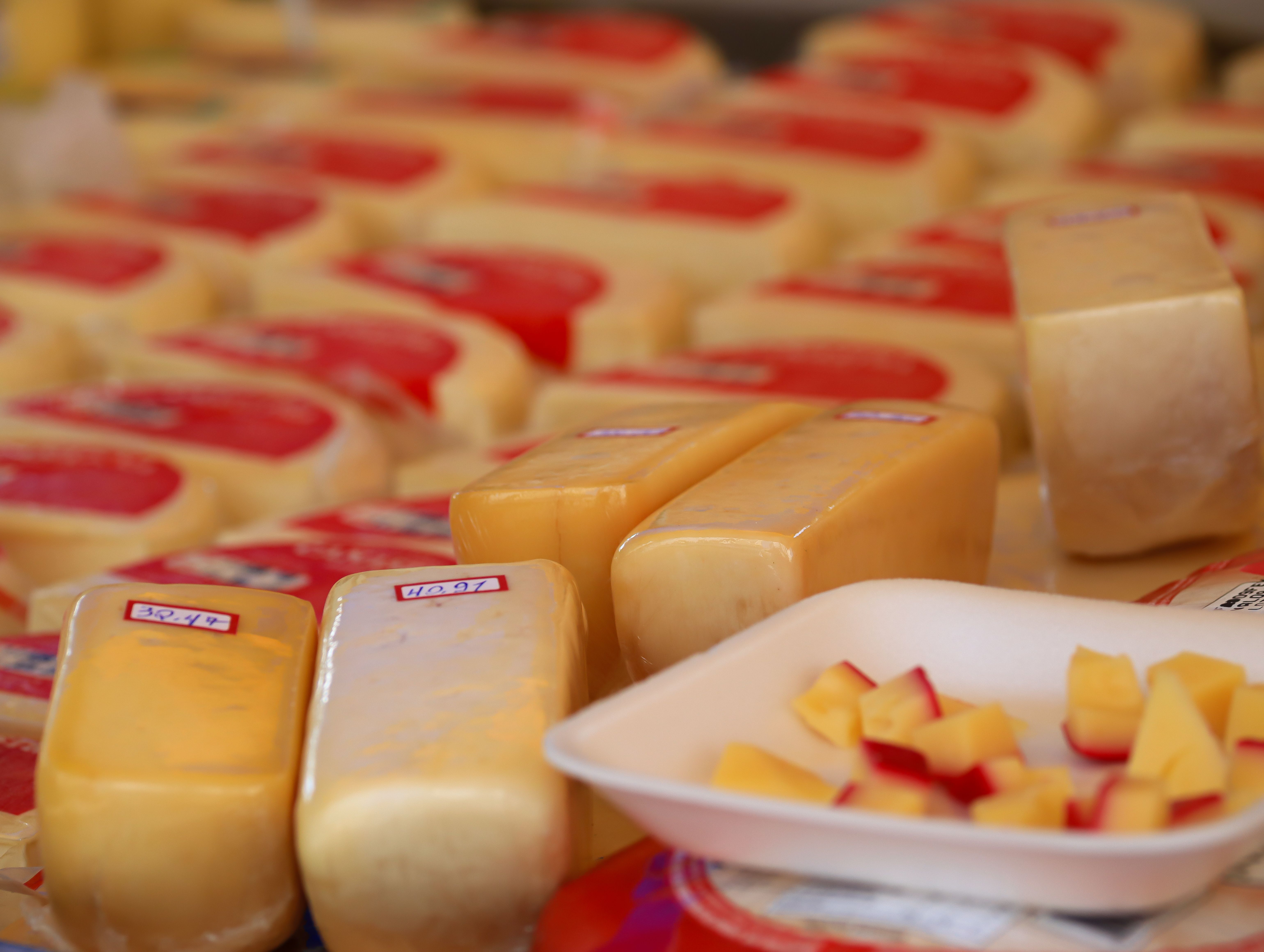 Variety of cheese blocks and samples on display at a market stall.